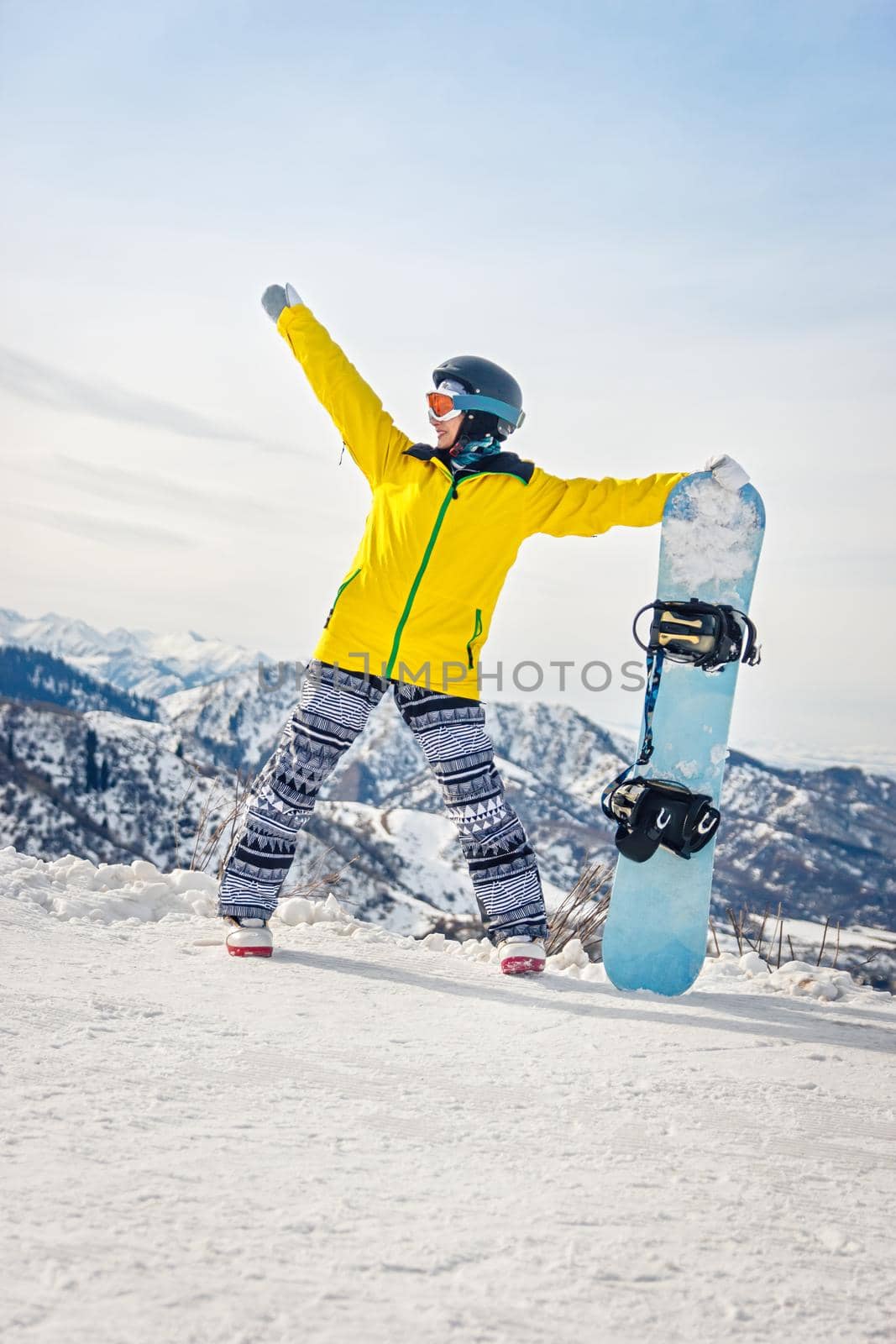 Young woman snowboarder in a yellow jacket and black helmet on the background of snowy mountains