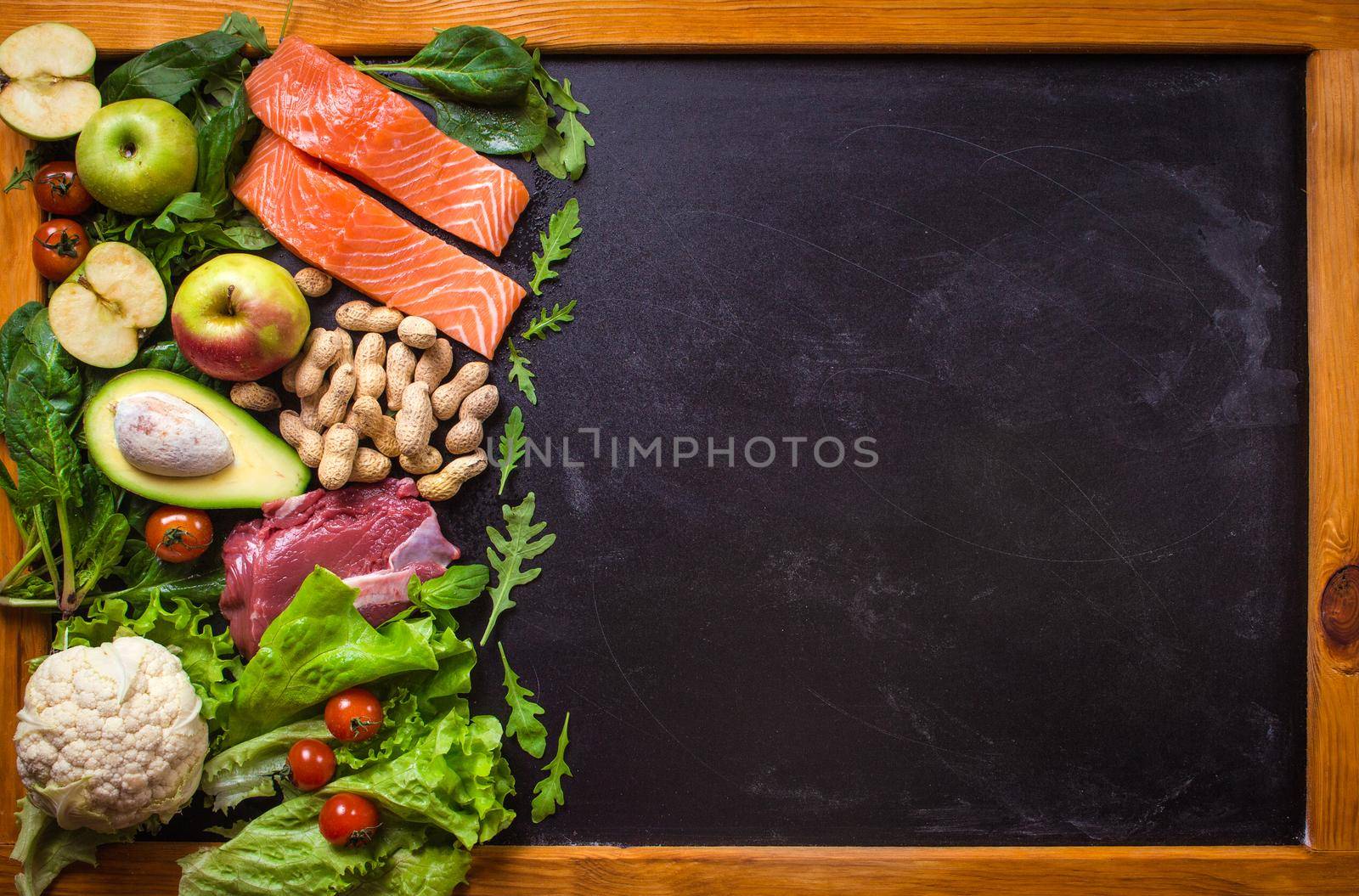 Fresh vegetables, fruits, fish, meat, nuts on black chalk board background. Сauliflower, avocado, apples, tomatoes, salmon, beef, spinach, herbs. Diet/healthy/paleo food. Ingredients. Space for text
