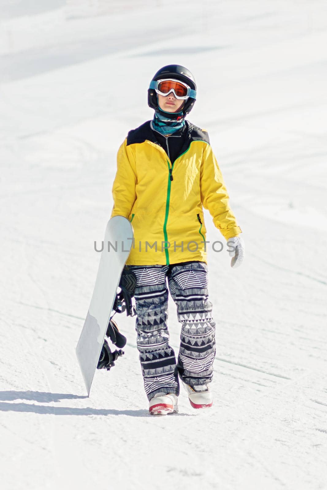 Young woman with snowboard in hand walking on ski slope, she's looking at camera, copy space