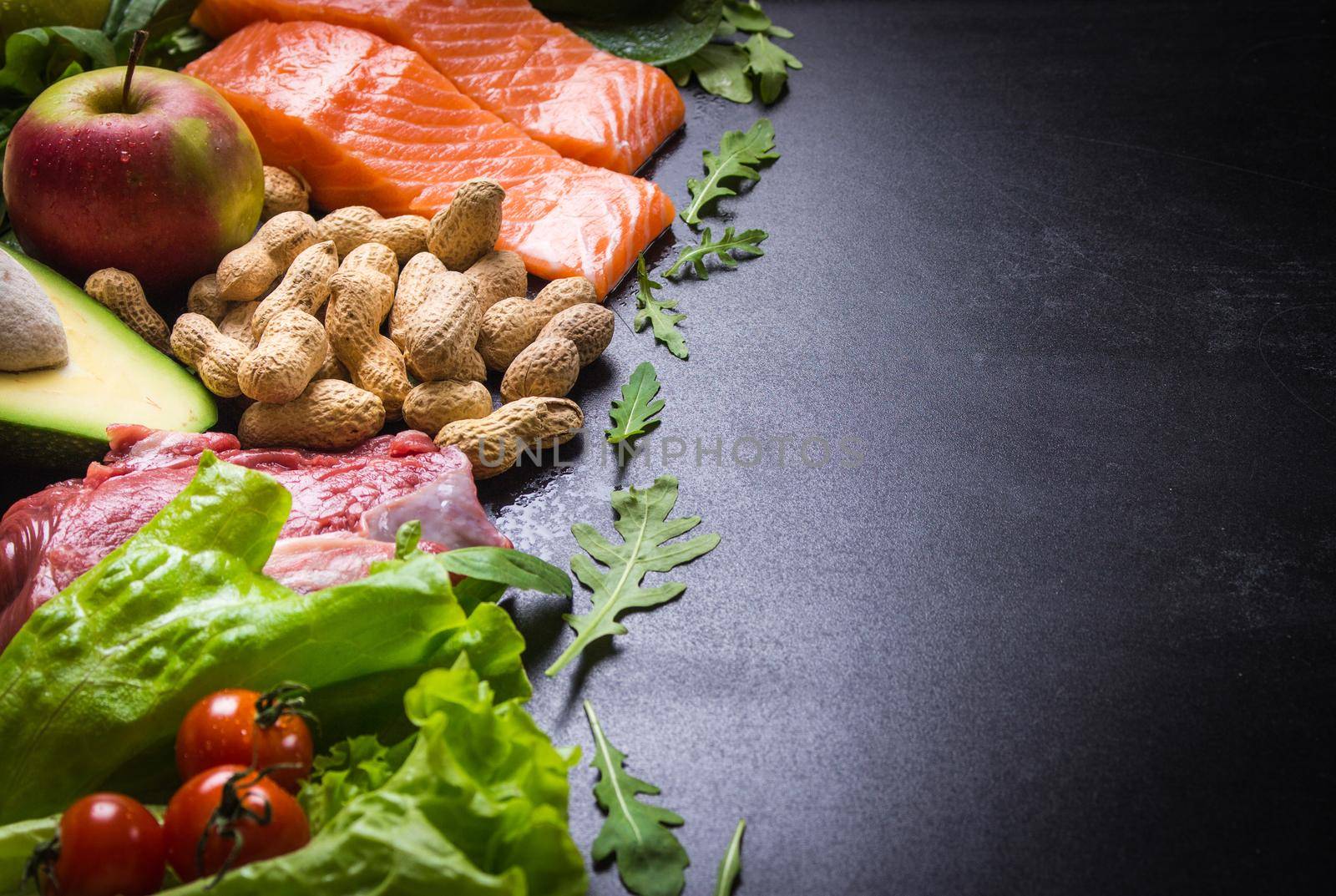 Fresh vegetables, fruits, fish, meat, nuts on black chalk board background. Сauliflower, avocado, apples, tomatoes, salmon, beef, spinach, herbs. Diet/healthy/paleo food. Ingredients. Space for text