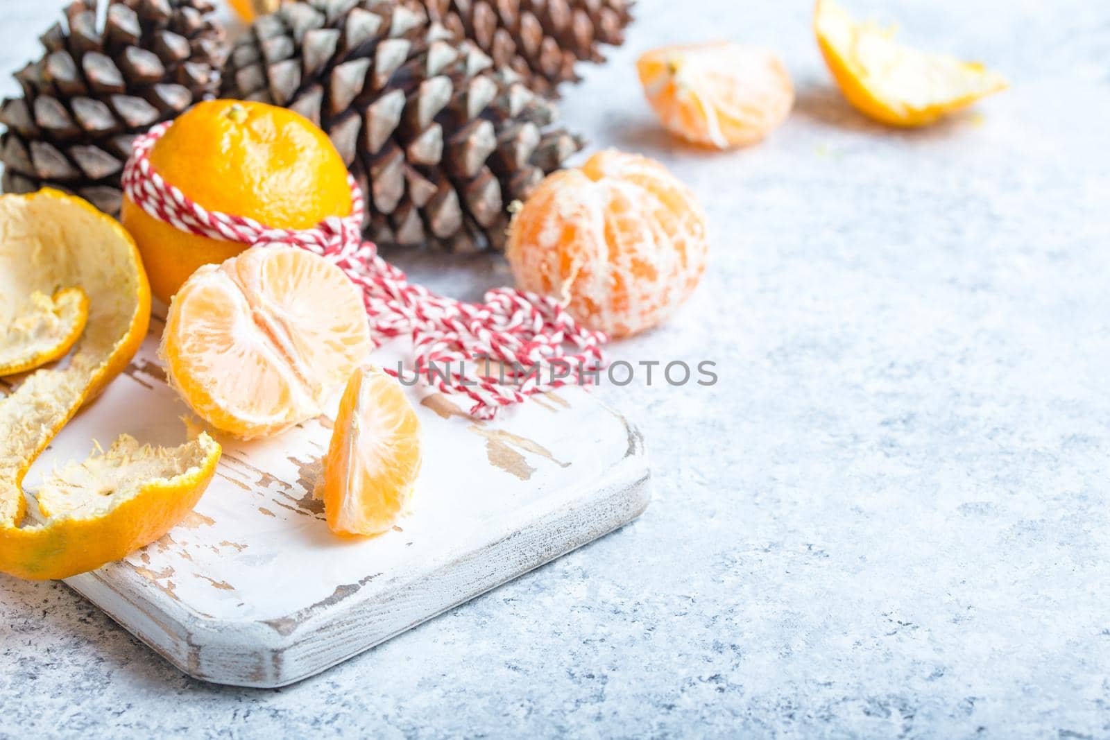 Winter white christmas background, tangerines, pine cones. Peeled tangerine, white cooking board. New Year/Xmas festive background. Winter holidays. Decoration, celebration Christmas. Space for text