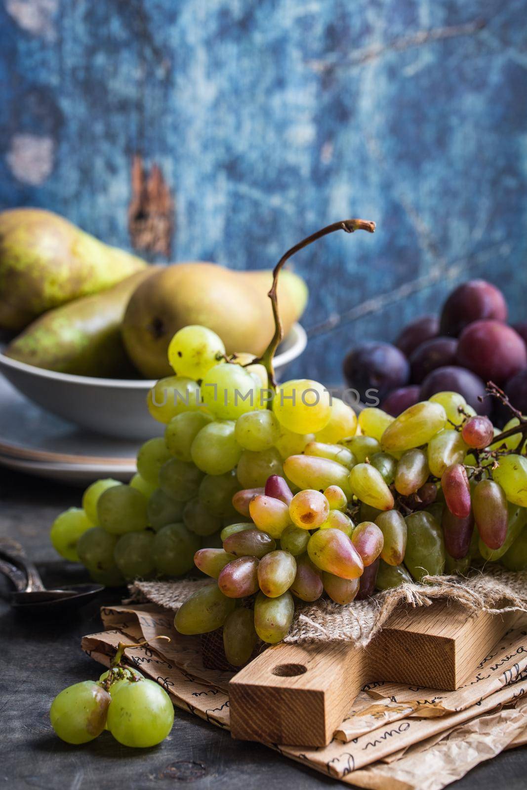 Fresh ripe grapes on wooden cutting board, pears and plums in bowls, wooden rustic background. Fresh juicy organic fruits. Close up. Organic natural fruits. Autumn/fall setting. Harvest/crop/garden