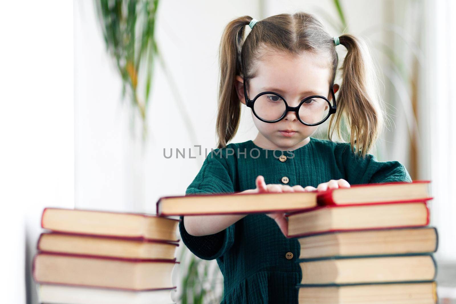 Caucasian little child girl in green dress and glasses procrastination while reading book. Home work and preschool education concept