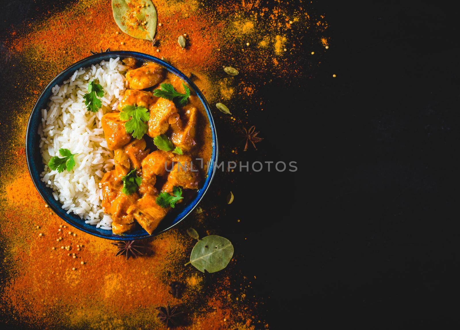 Indian Butter chicken with basmati rice in bowl, spices, black background. Space for text. Butter chicken, traditional Indian dish. Top view. Chicken tikka masala. Indian cuisine concept. Overhead