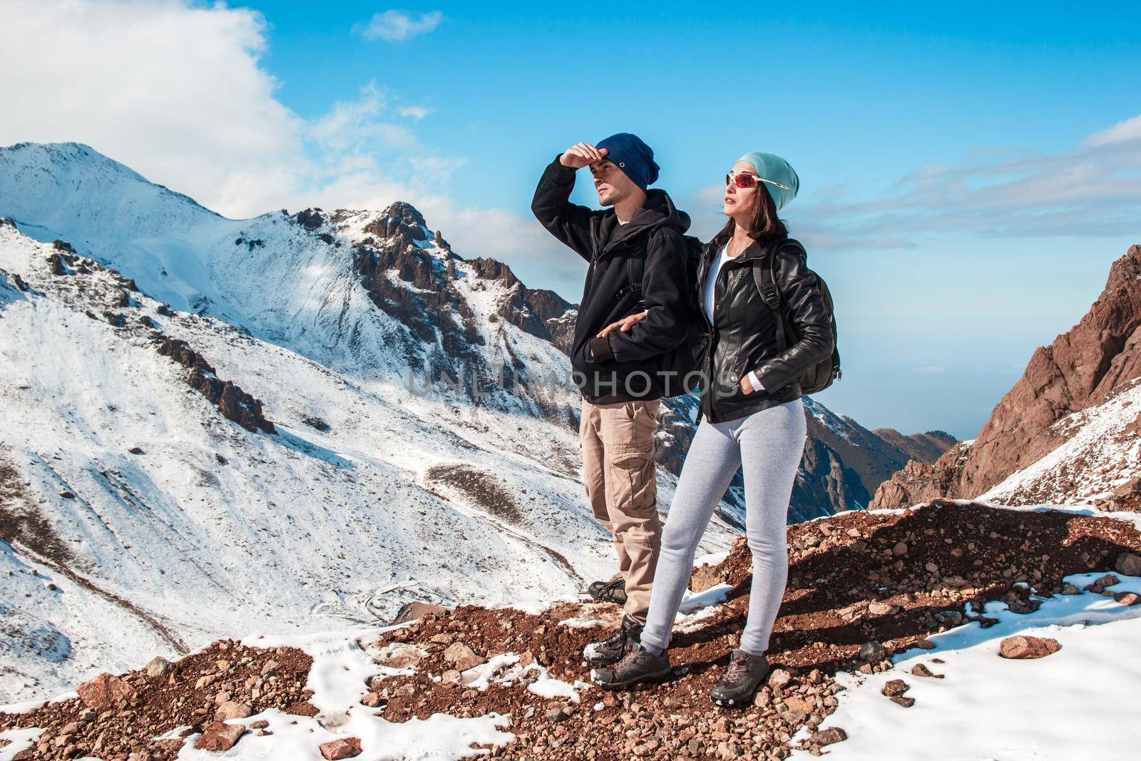 A man and a woman stand in a mountain gorge amid snow slopes.