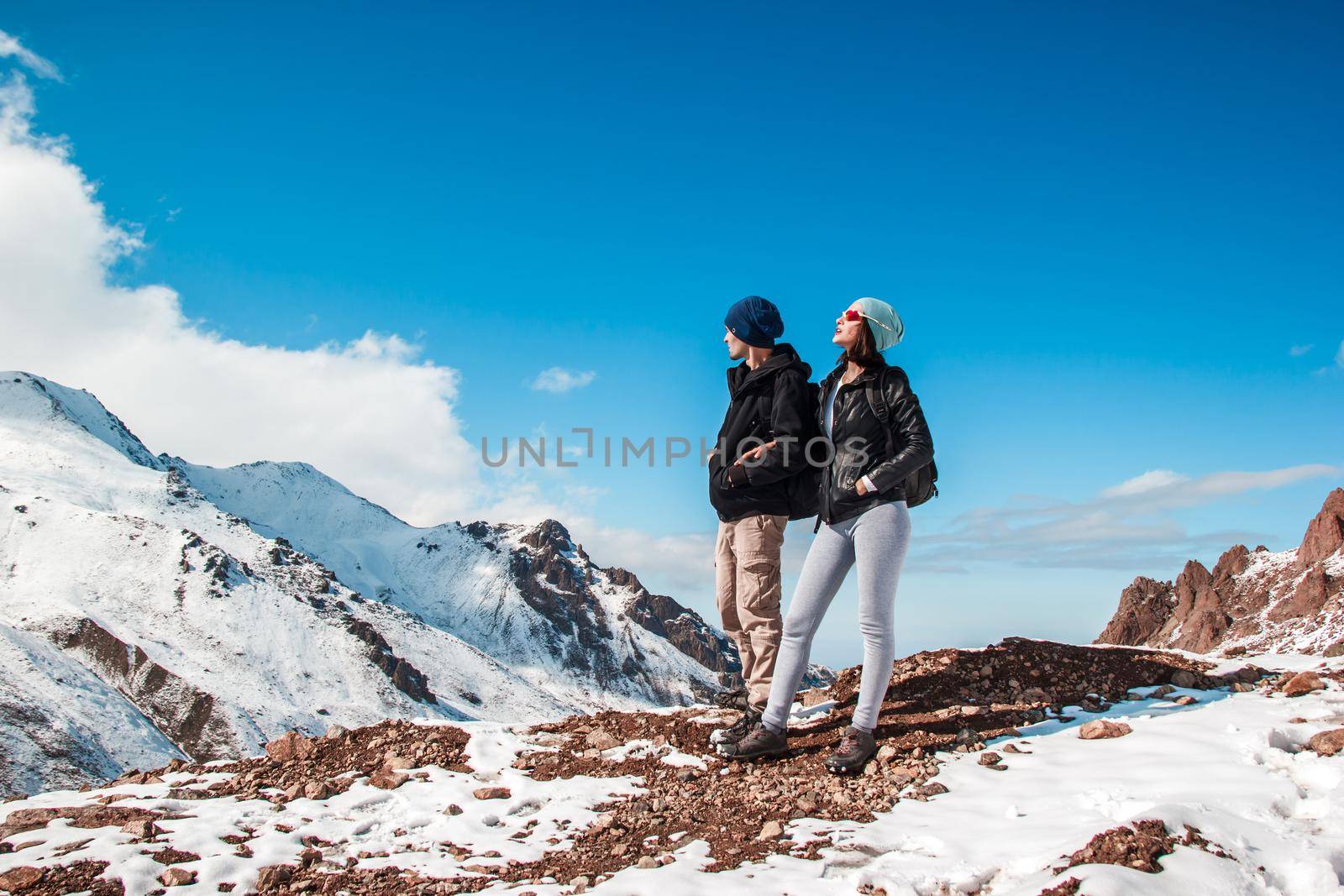 A guy and a girl stand on a mountain slope against the background of a blue sky.