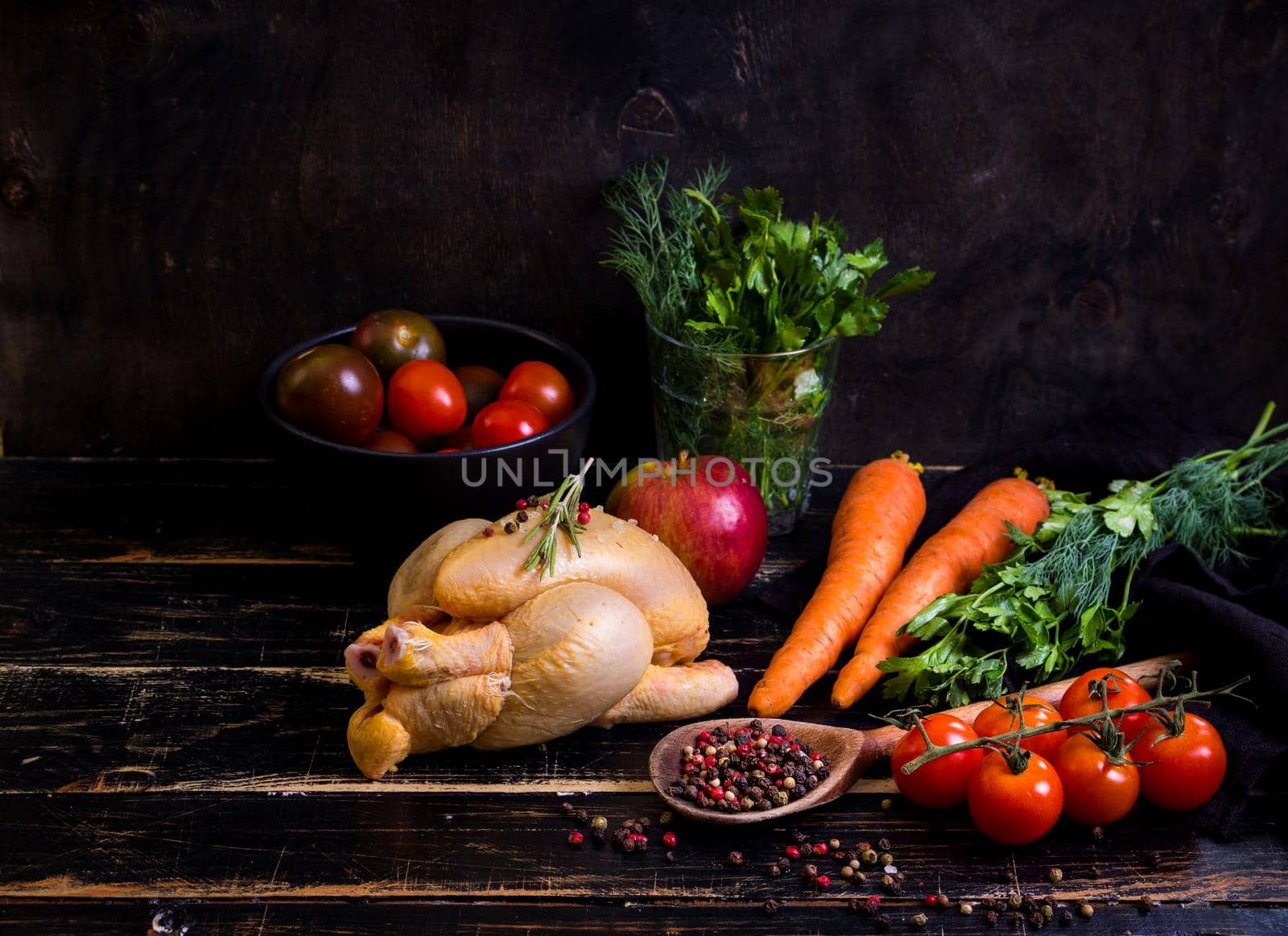 Raw whole chicken ready for cooking. Chicken with vegetables, herbs and spices on a black rustic wooden background. Diet or clean healthy eating concept. Ingredientd for cooking