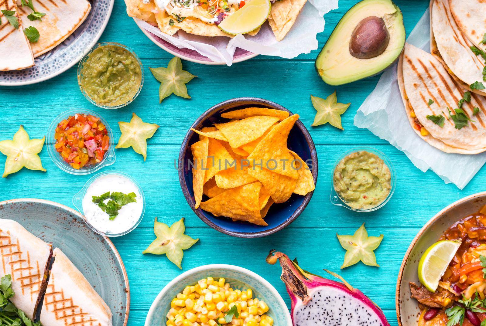 Assorted mix of traditional Mexican food. Different Mexican dishes table. Cheese nachos, tacos, guacamole, quesadilla, burrito, fajitas, tortilla chips, Mexican fruits. Tex-Mex cuisine. Mexico style