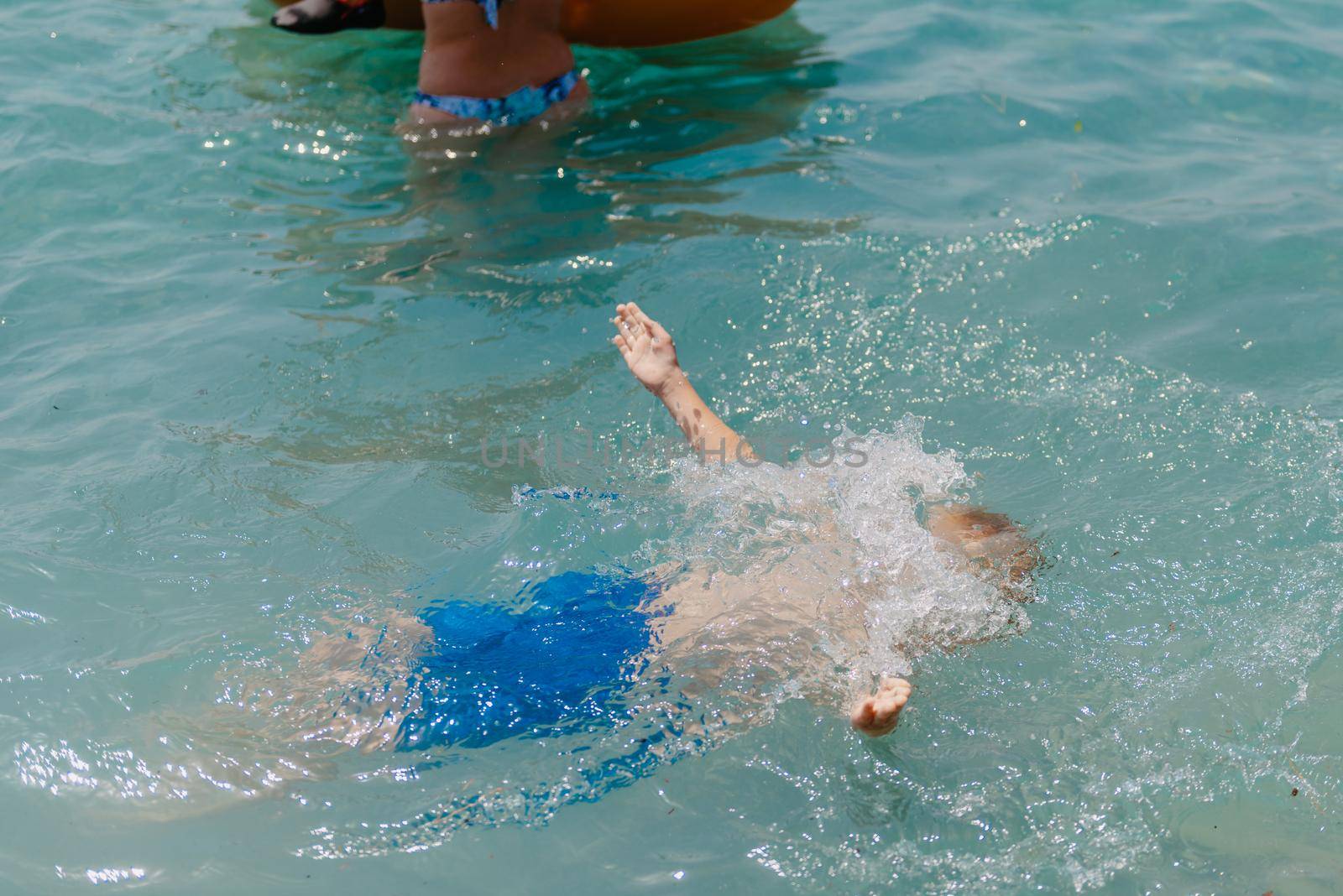 Child learning to swim in the open sea of tropical resort. Kids learn swimming. Exercise and training for young children. Little boy with colorful float board in sport club. Swimming baby or toddler. Happy child boy swims in sea in swimming circle with splash. Blue sky and water. Swimming training. Fun joy activities on vacation in the beach. Childhood moments lifestyle. Freedom careless. boy swim in the sea.