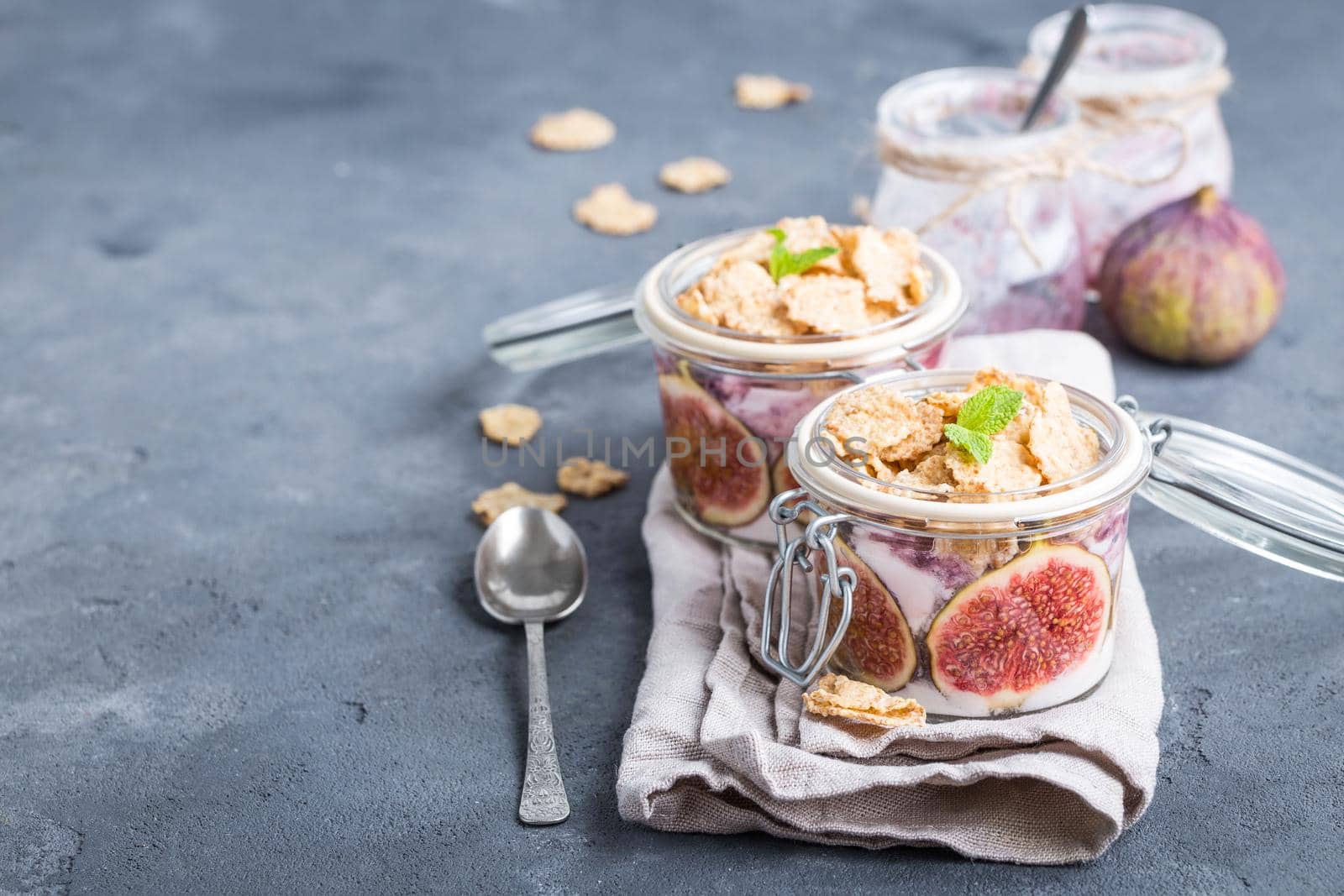 Homemade healthy yoghurt in glass pot with cereals, figs, mint on rustic stone background. Space for text. Healthy morning breakfast. Freshly made yoghurt, oat granola and fruit. Healthy eating