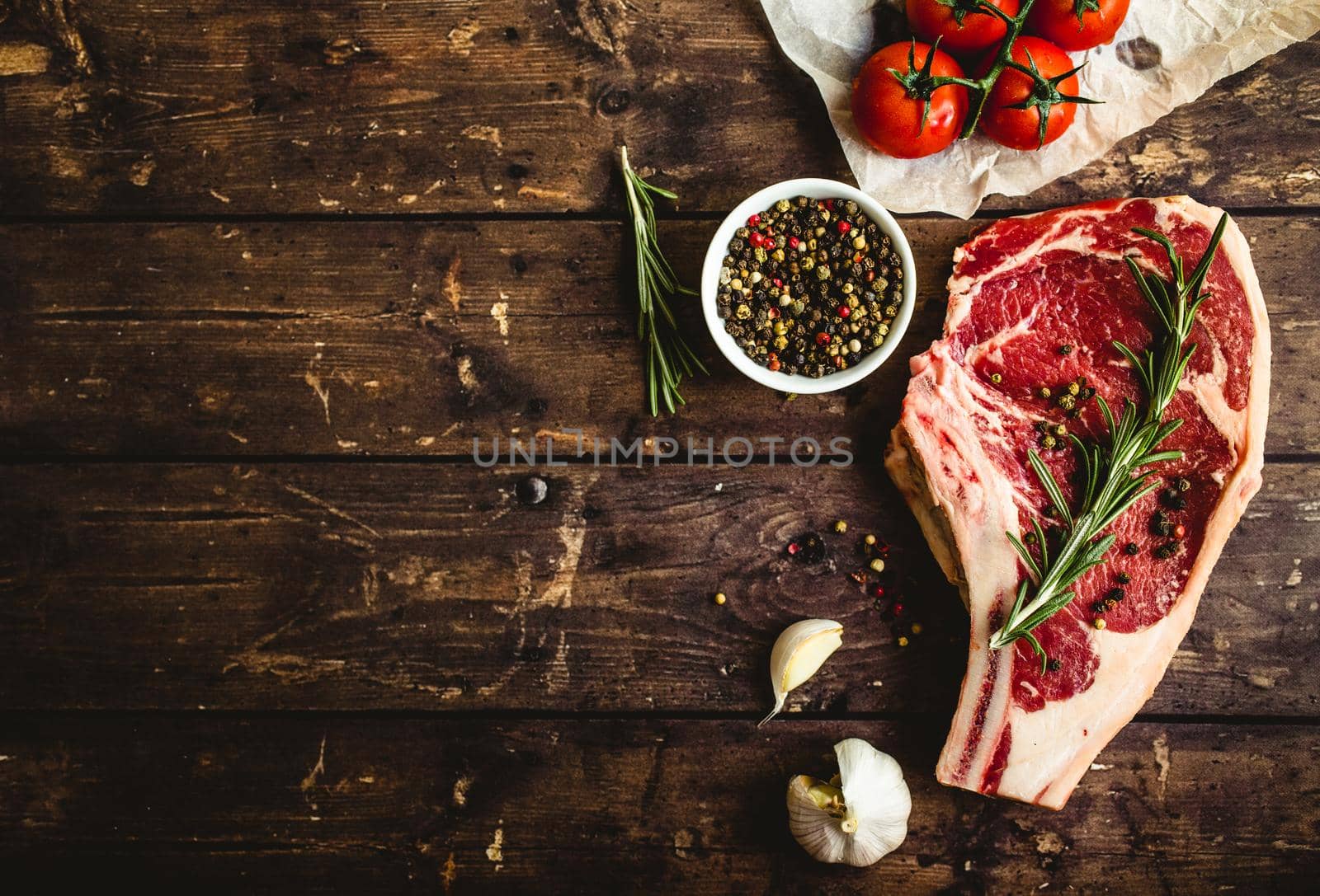 Raw marbled meat steak, pepper, herbs, tomato, old wooden background. Space for text. Beef Rib eye steak ready for cooking. Top view. Copy space. Ingredients, meat roasting. Ribeye meat steak. Closeup