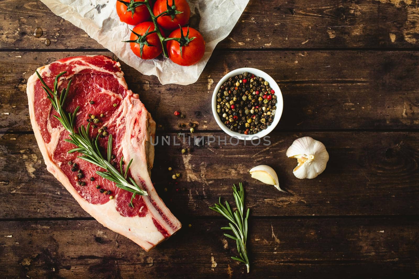 Raw marbled meat steak, pepper, herbs, tomatoes, old wooden table background. Beef Rib eye steak ready for cooking. Top view. Ingredients ready for meat roasting. Uncooked Ribeye meat steak. Closeup