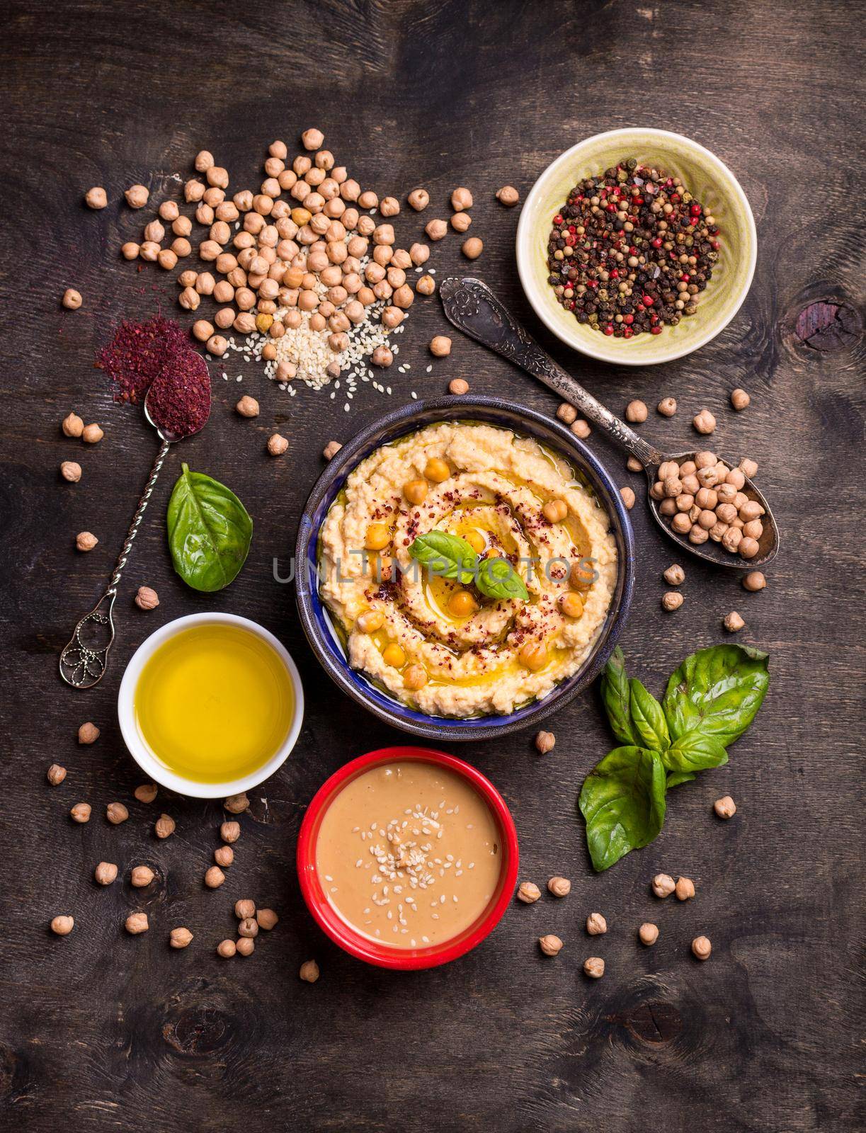 Hummus ingredients. Chickpea, tahini paste, olive oil, sesame seeds, sumac, herbs on dark rustic wooden background. Set of raw ingredients for making hummus. Middle eastern cuisine. Top view