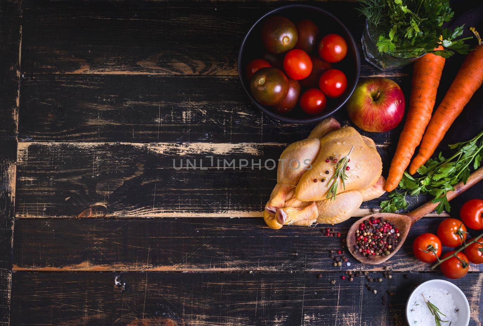 Raw whole chicken ready for cooking. Chicken with vegetables, herbs and spices on a black rustic wooden background. Space for text. Food frame. Diet or healthy eating. Ingredientd for cooking