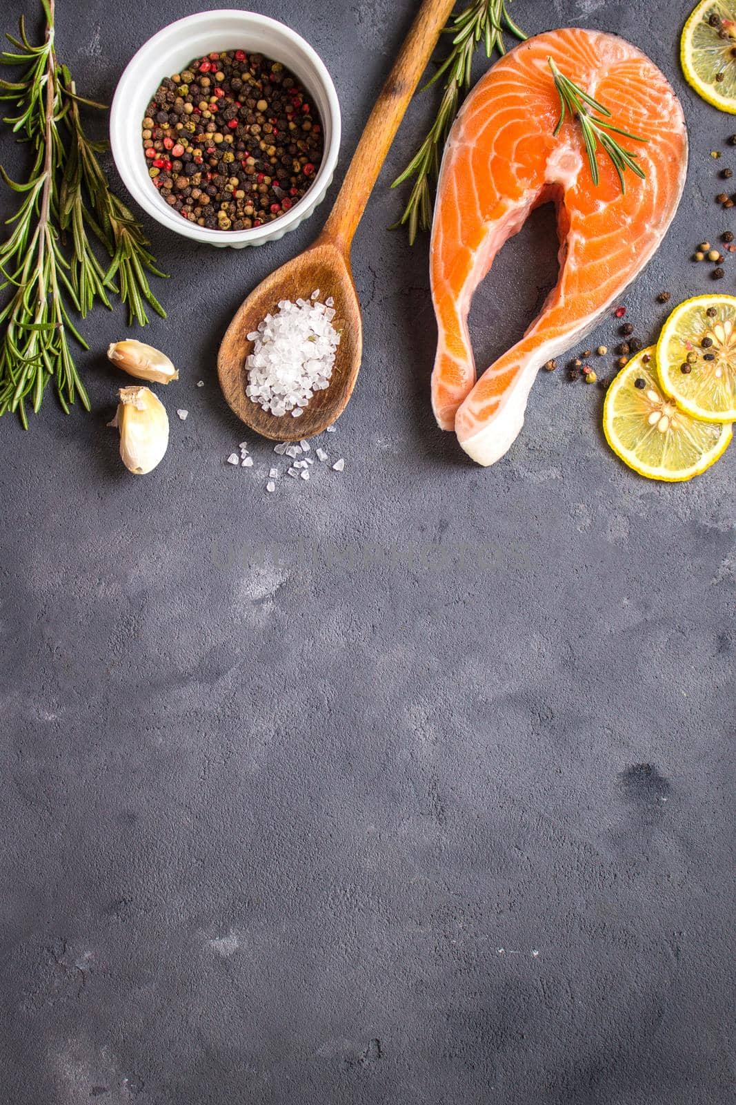 Fresh raw salmon steak, lemon, herbs, spices, wooden spoon on dark rustic concrete background. Food frame. Ingredients set for making healthy dinner. Healthy/diet concept. Space for text. Fresh fish