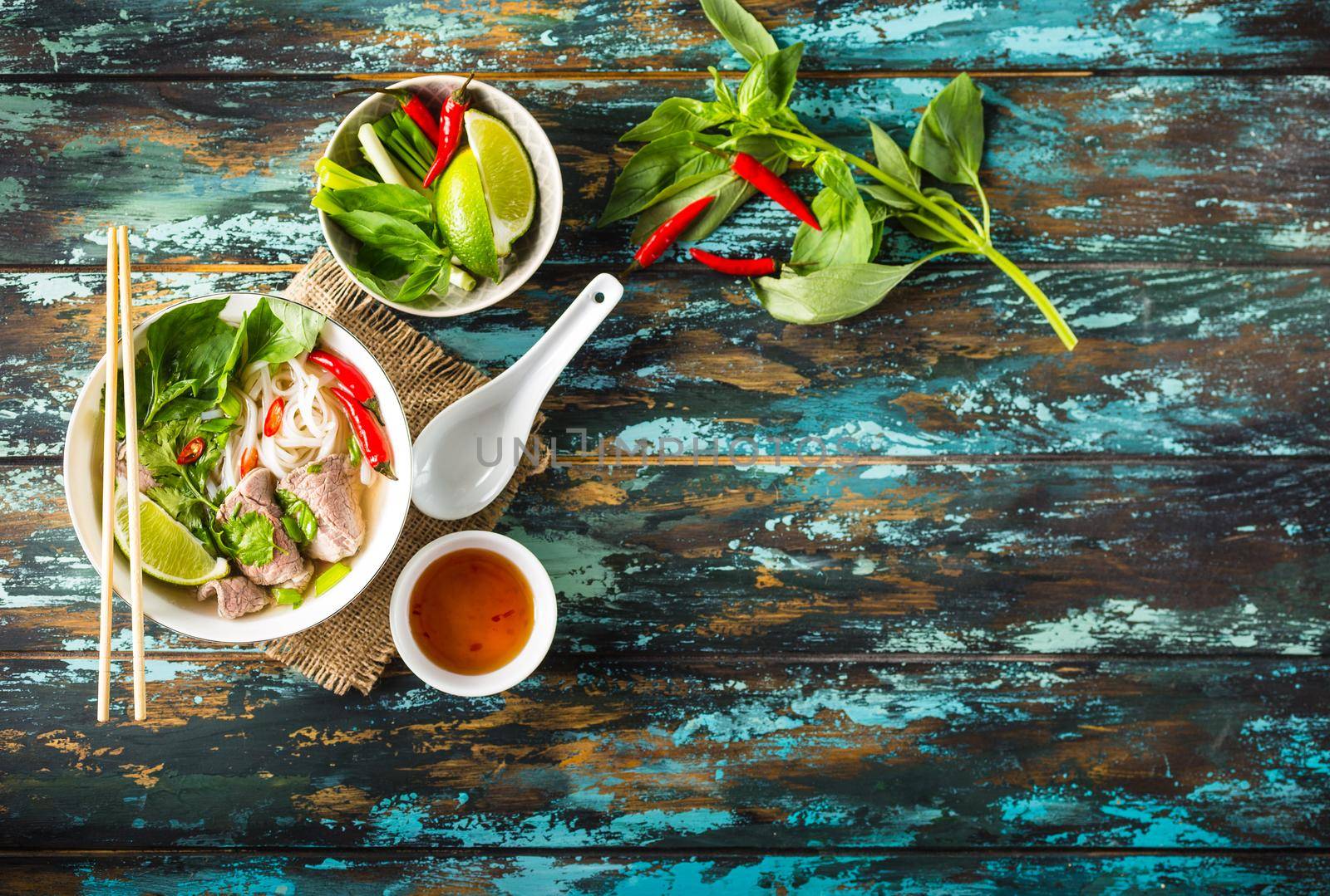 Traditional Vietnamese soup Pho bo with herbs, meat, rice noodles, broth. Pho bo in bowl with chopsticks, spoon. Space for text. Top view. Asian soup Pho bo on wooden table background. Vietnamese soup