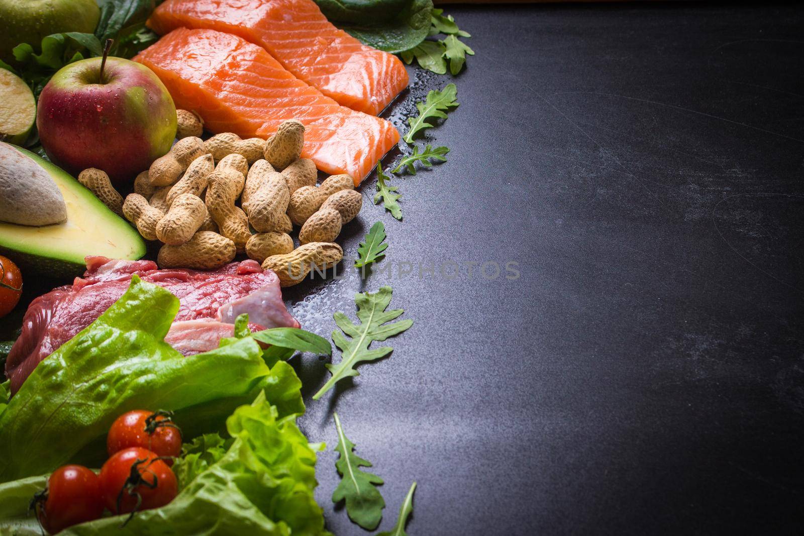 Fresh vegetables, fruits, fish, meat, nuts on black chalk board background. Сauliflower, avocado, apples, tomatoes, salmon, beef, spinach, herbs. Diet/healthy/paleo food. Ingredients. Space for text