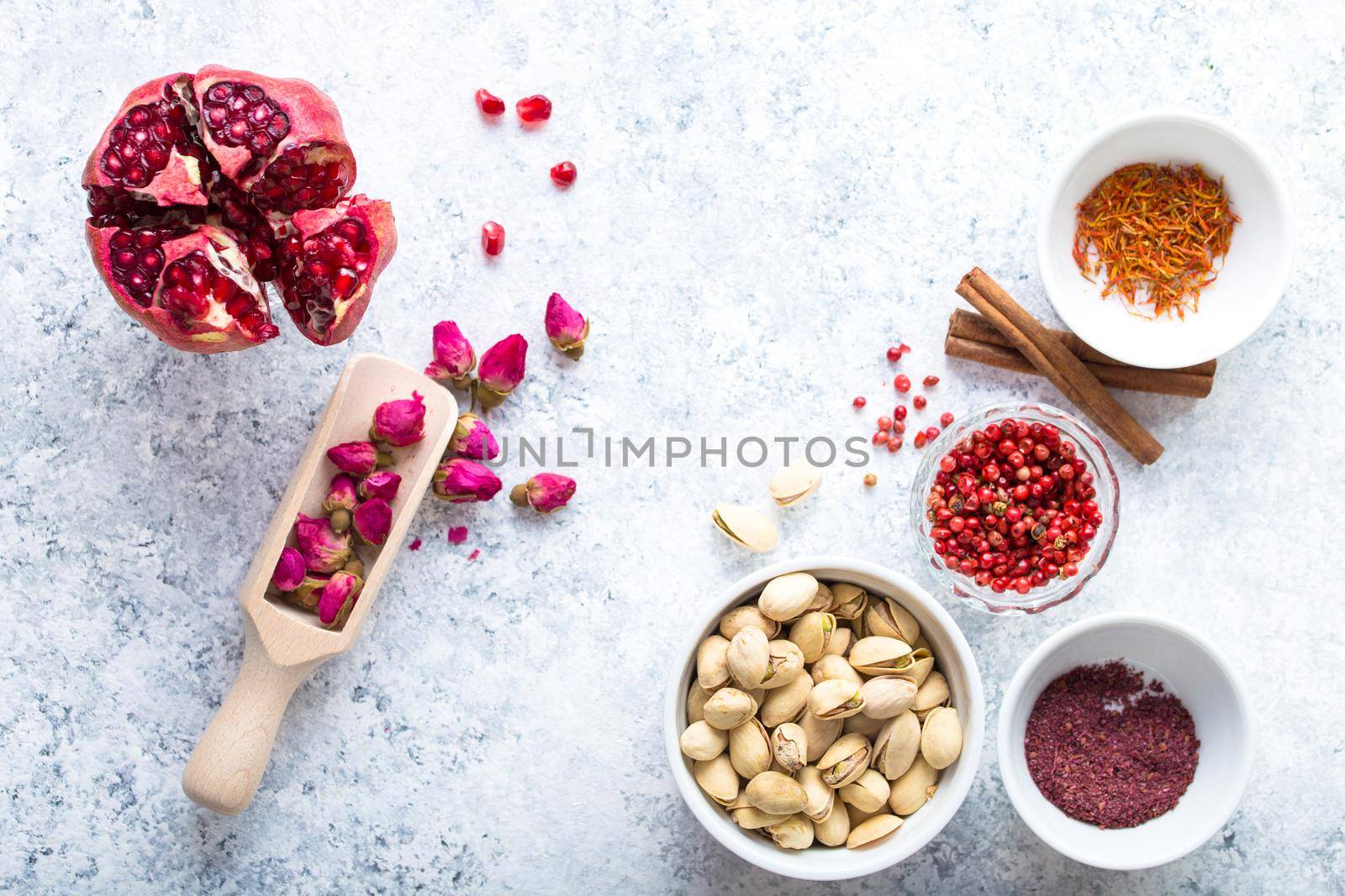 Arab ingredients, middle eastern food. Space for text. Arabic cuisine ingredients, white concrete background. Rose buds, spices, pomegranate, pistachios. Halal food making. Top view. Arab food concept