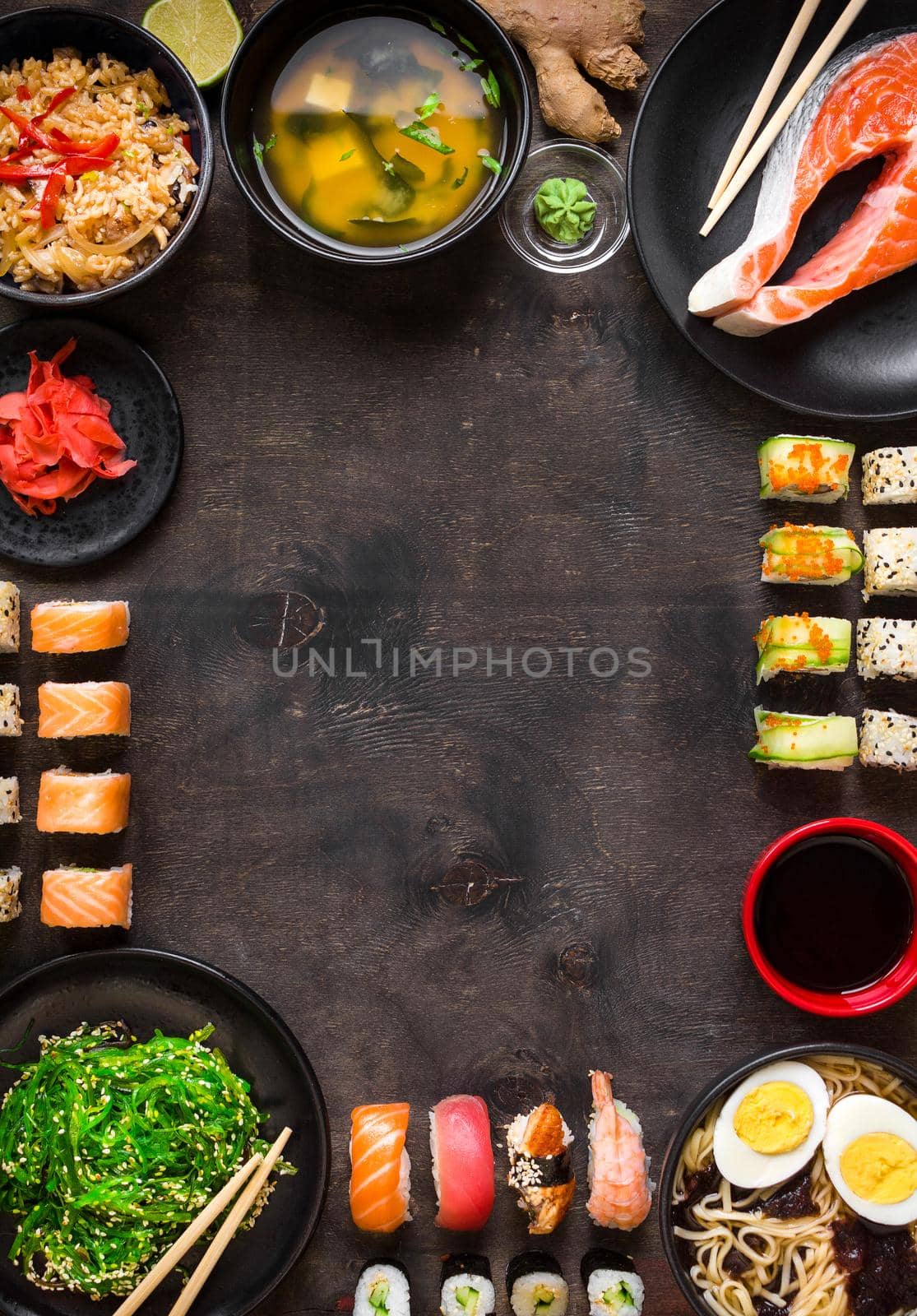 Sushi and japanese food on dark background. Sushi rolls, hiyashi wakame, miso soup, ramen, fried rice with vegetables, nigiri, salmon steak, soy sauce, сhopsticks. Asian/Japanese food frame. Overhead....