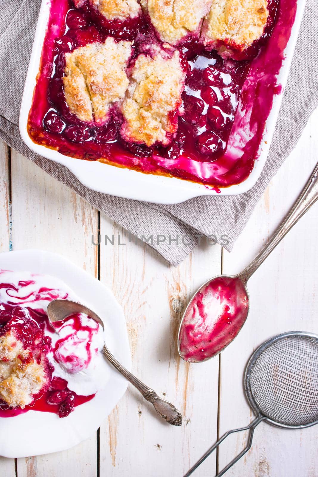 Homemade cherry cobbler pie with flaky crust, ice cream, vintage spoon, sieve for flour. Top view on the white wooden table.