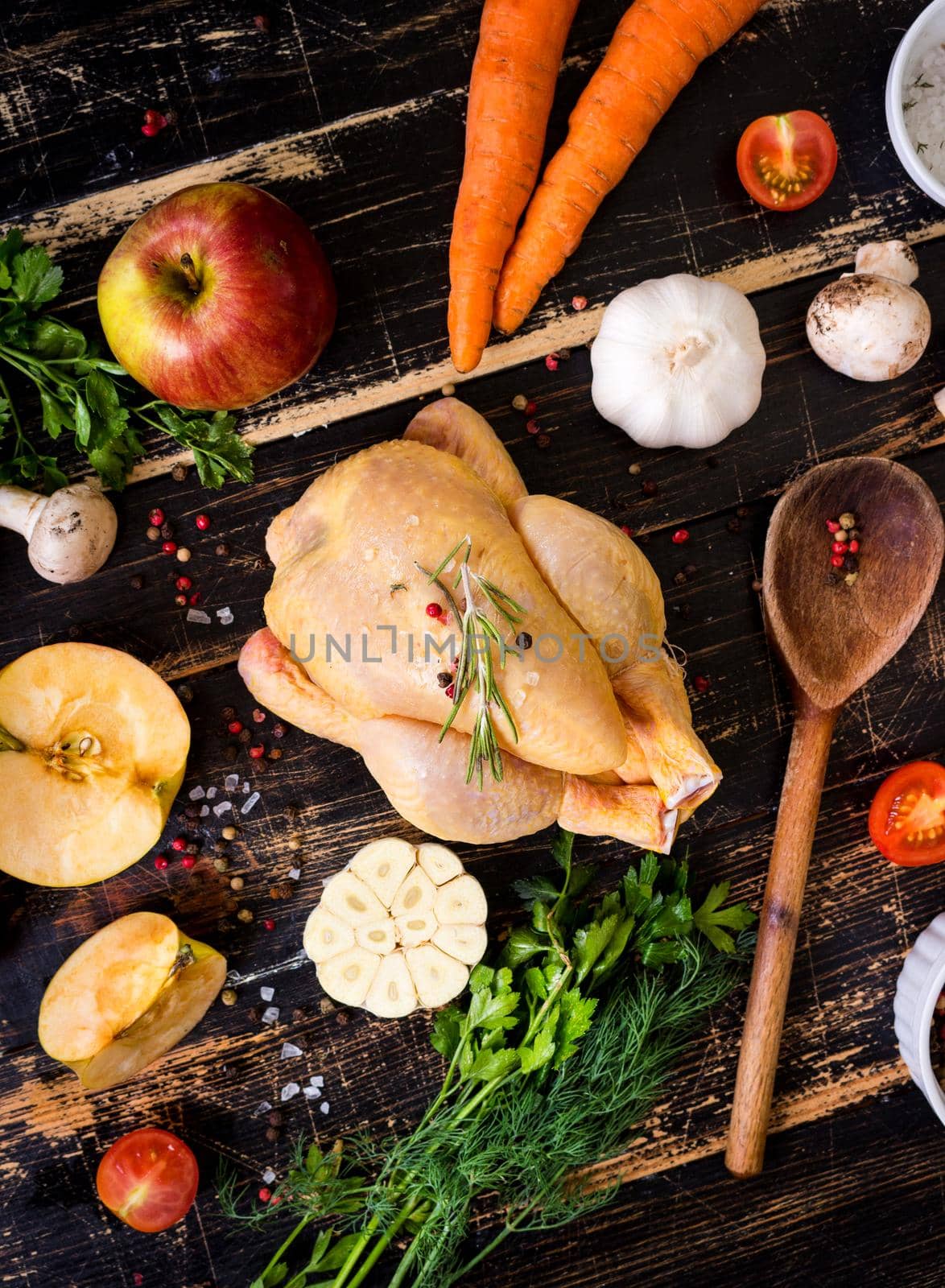 Raw whole chicken ready for cooking. Chicken with vegetables, herbs and spices on a black rustic wooden background. Diet or clean healthy eating concept. Ingredientd for cooking