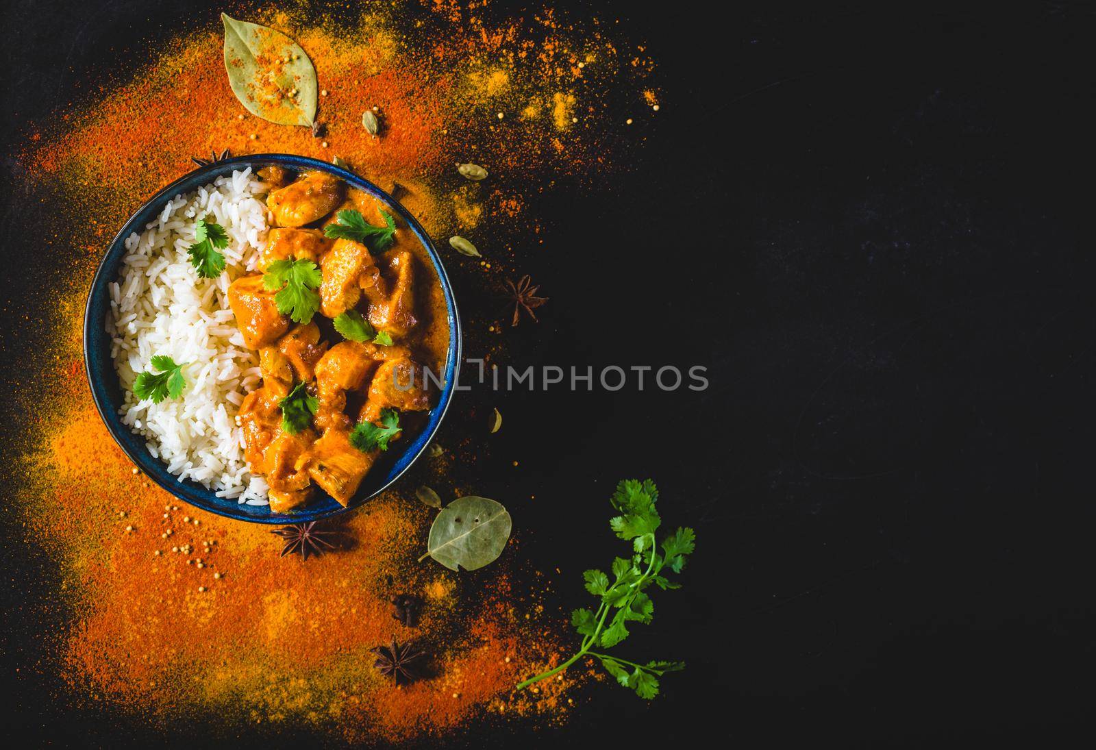 Indian Butter chicken with basmati rice in bowl, spices, black background. Space for text. Butter chicken, traditional Indian dish. Top view. Chicken tikka masala. Indian cuisine concept. Overhead