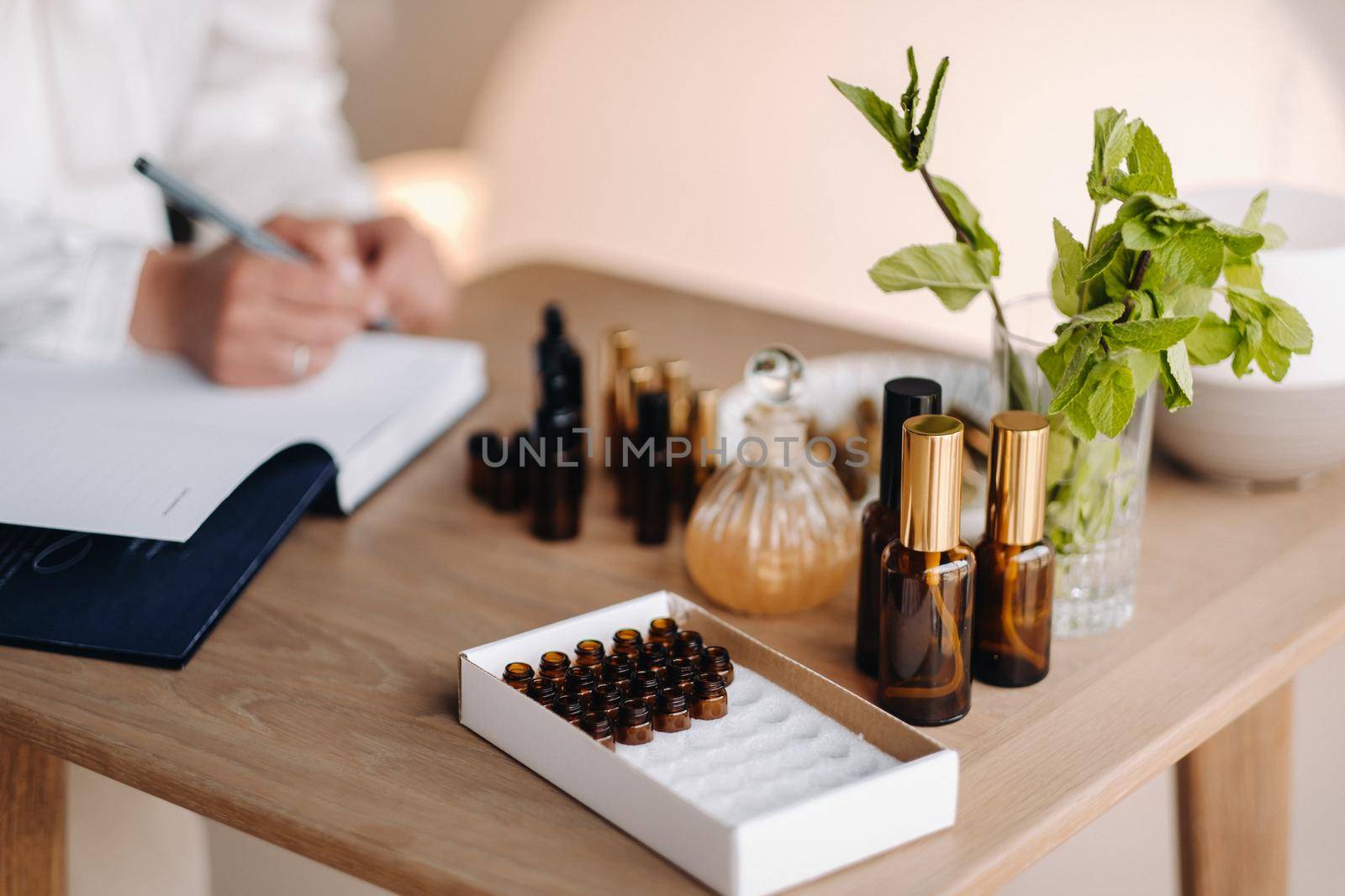 A close-up of bottles of essential oil and an aromatherapist writing a note in a notebook.