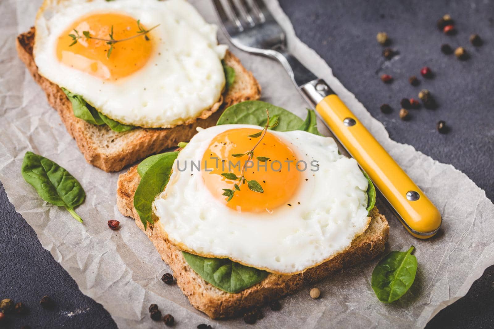 Healthy sandwich with wholegrain toast, fried egg, fresh spinach, thyme on rustic stone background. Egg sandwich for morning breakfast. Clean healthy eating concept. Vegetarian lunch/snack. Close-up