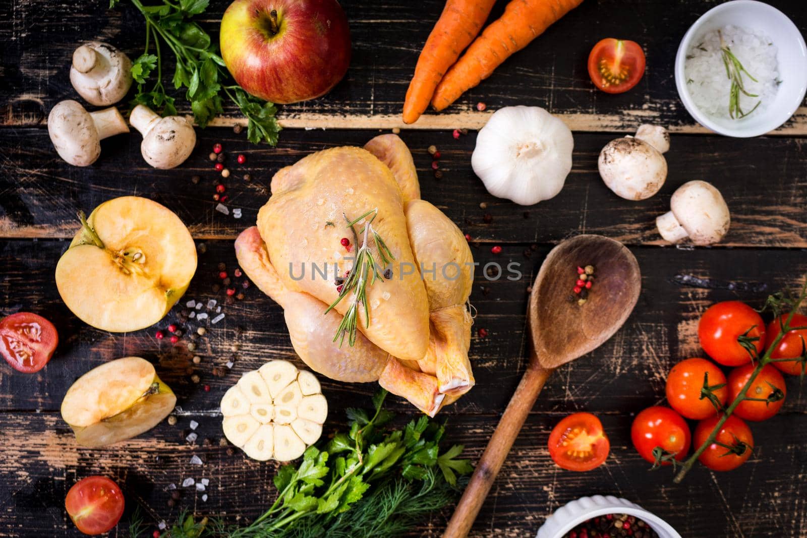 Raw whole chicken ready for cooking. Chicken with vegetables, herbs and spices on a black rustic wooden background. Diet or clean healthy eating concept. Ingredientd for cooking