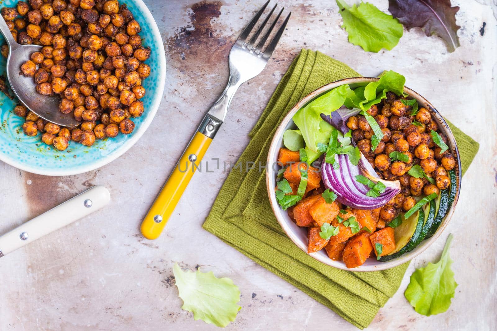 Healthy vegetarian salad with vegetables, sweet potato, chickpea, salad leaves. Healthy buddha bowl salad, sauce, fork. Vegan or vegetarian food. Healthy lunch/dinner. Salad in bowl on table. Top view