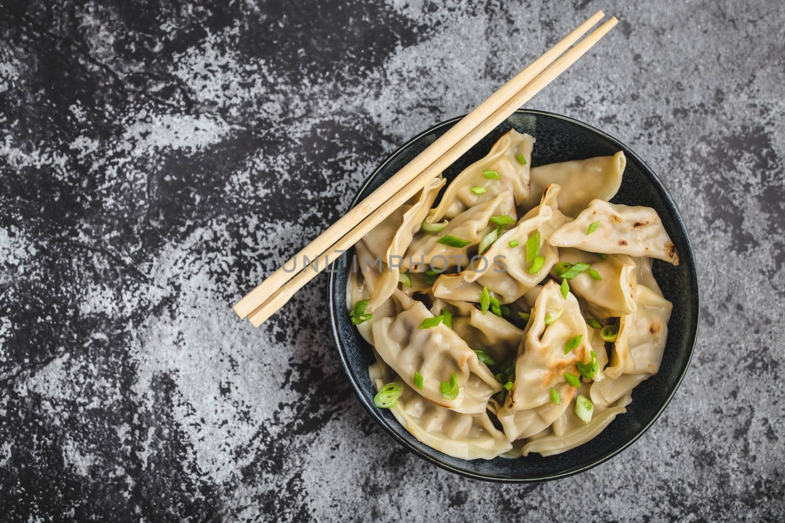 Asian dumplings in bowl, chopsticks, rustic stone background. Top view. Chinese dumplings for dinner. Closeup. Chinese dumplings for dinner/lunch. Traditional Asian/Chinese cuisine. Overhead. Dim sum