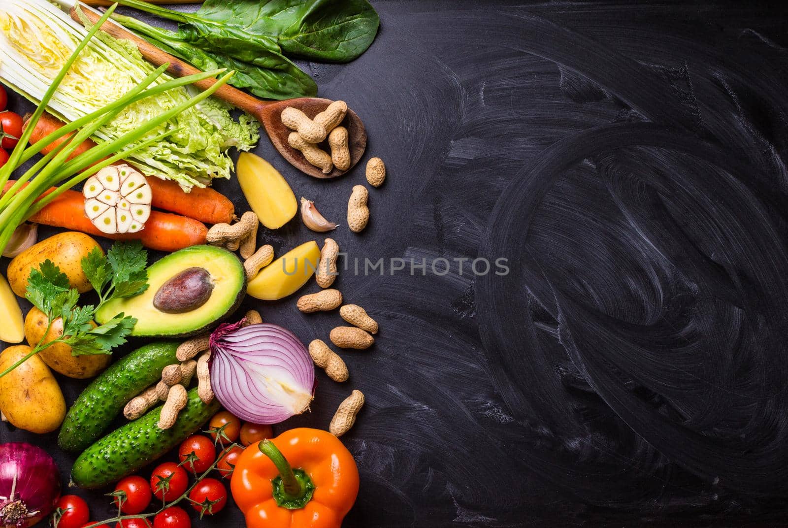 Vegetables, herbs, nuts, ingredients for cooking, wooden spoon on rustic black chalk board background. Healthy, clean eating concept. Vegan or gluten free diet. Space for text. Top view. Salad making