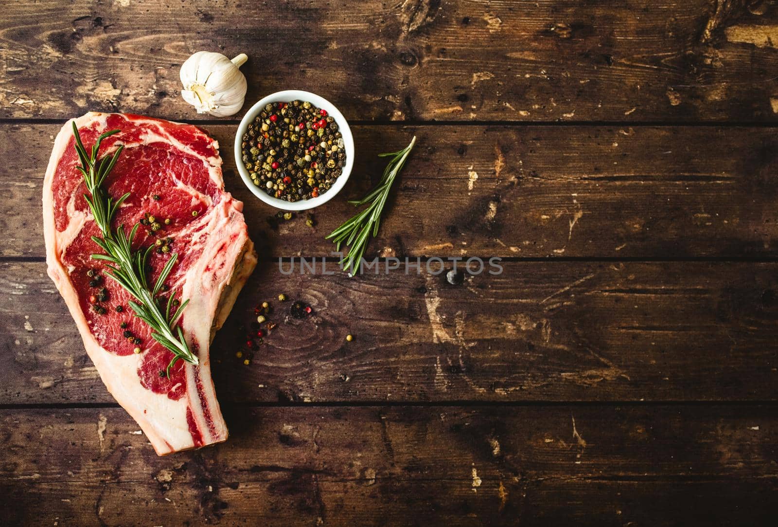 Raw marbled meat steak, pepper, herbs, garlic, old wooden background. Space for text. Beef Rib eye steak ready for cooking. Top view. Copy space. Ingredients, meat roasting. Ribeye meat steak. Closeup