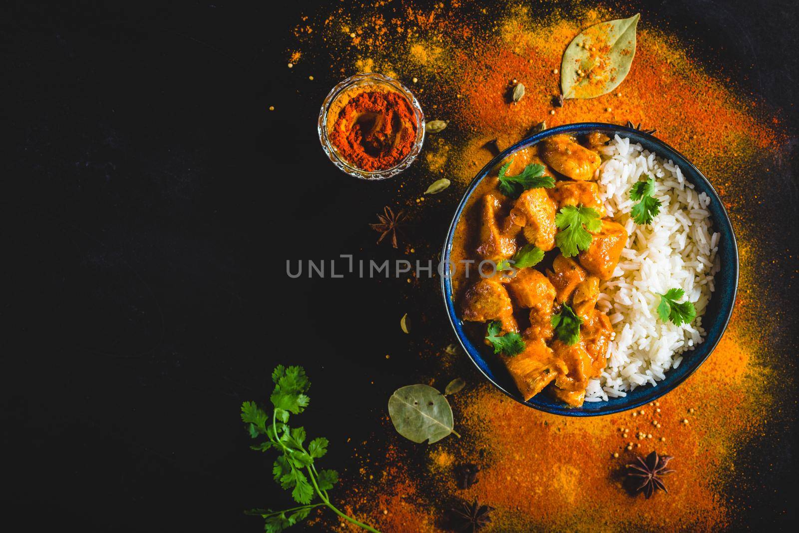 Indian Butter chicken with basmati rice in bowl, spices, black background. Space for text. Butter chicken, traditional Indian dish. Top view. Chicken tikka masala. Indian cuisine concept. Overhead