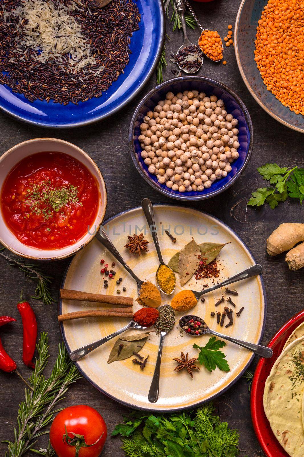 Assorted spices, herbs, chick-pea, lentil, basmati and wild rice mix, tomato chutney and pita on colorful plates. Top view. Spices and different food. Indian/ayurvedic food...