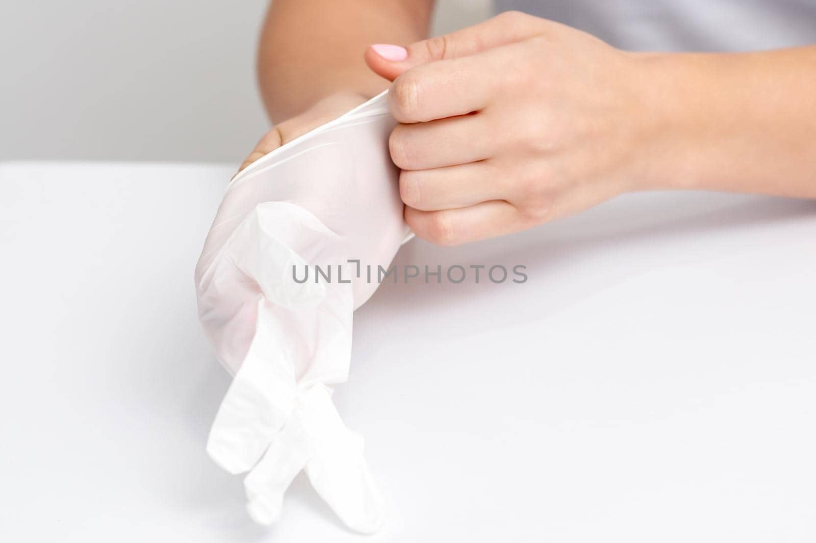 Woman hands is putting on the white rubber gloves in manicure salon.