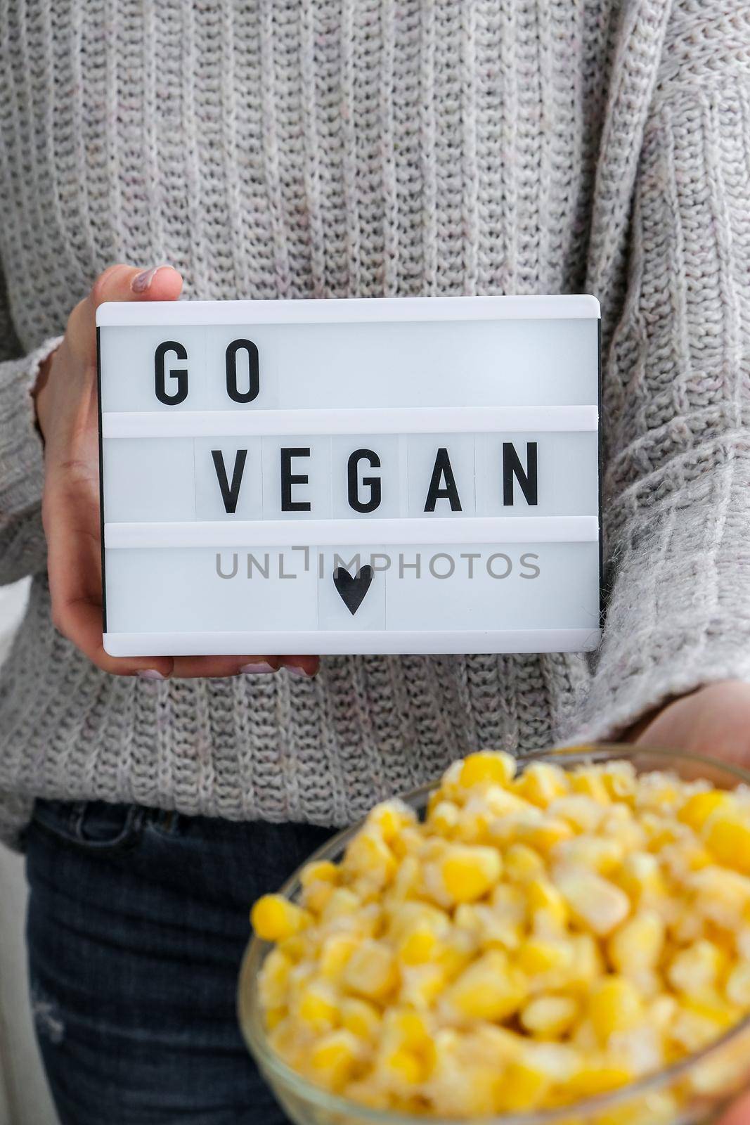 Lightbox with text GO VEGAN in female hands. Veganism, vegetarian healthy lifestyle. Frozen food in bowl. Healthy eating vegan. Yellow corn