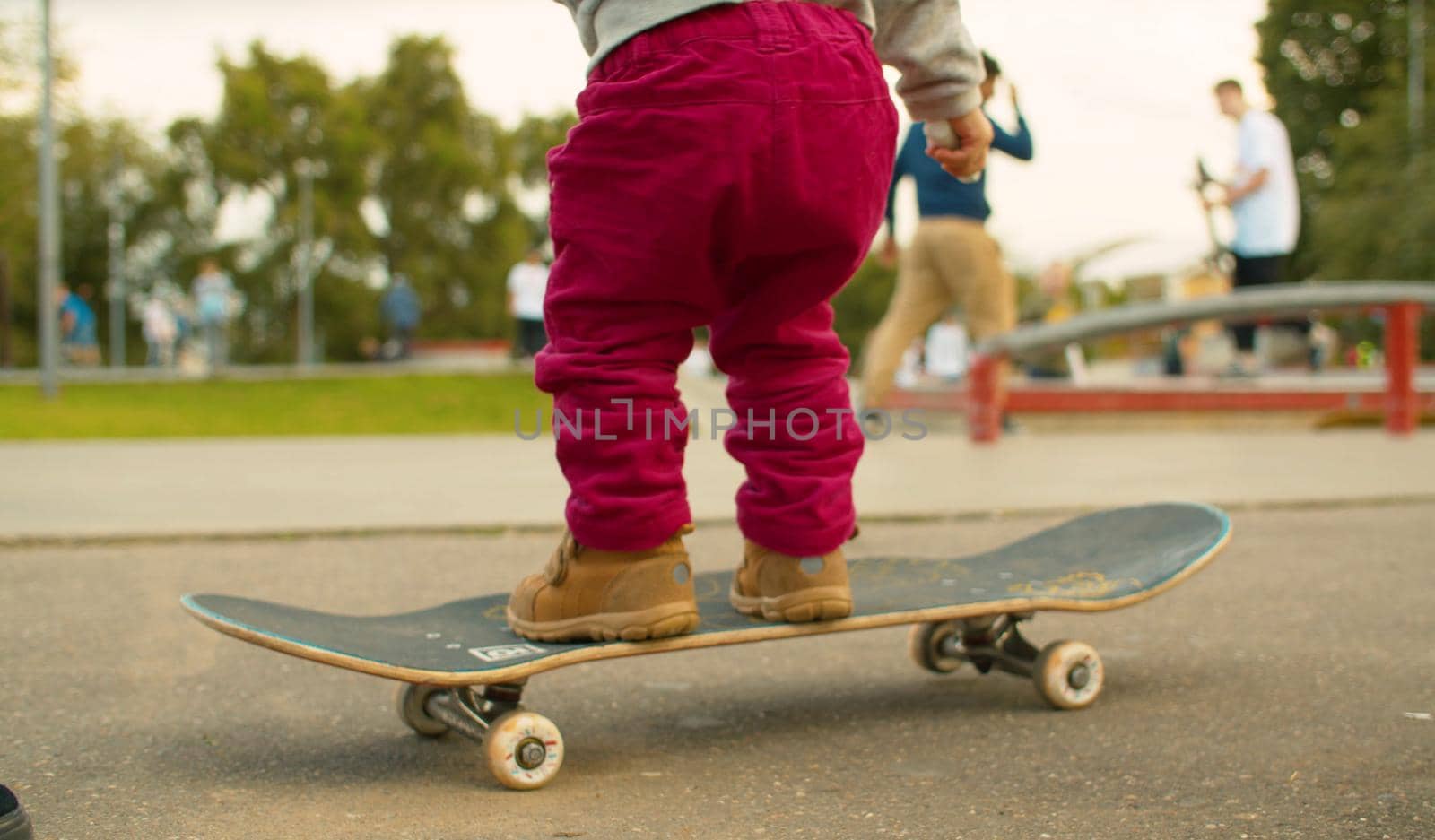 Legs of funny baby standing on a skate and trying to ride. Blurry unrecognizable people riding a skates in slow motion