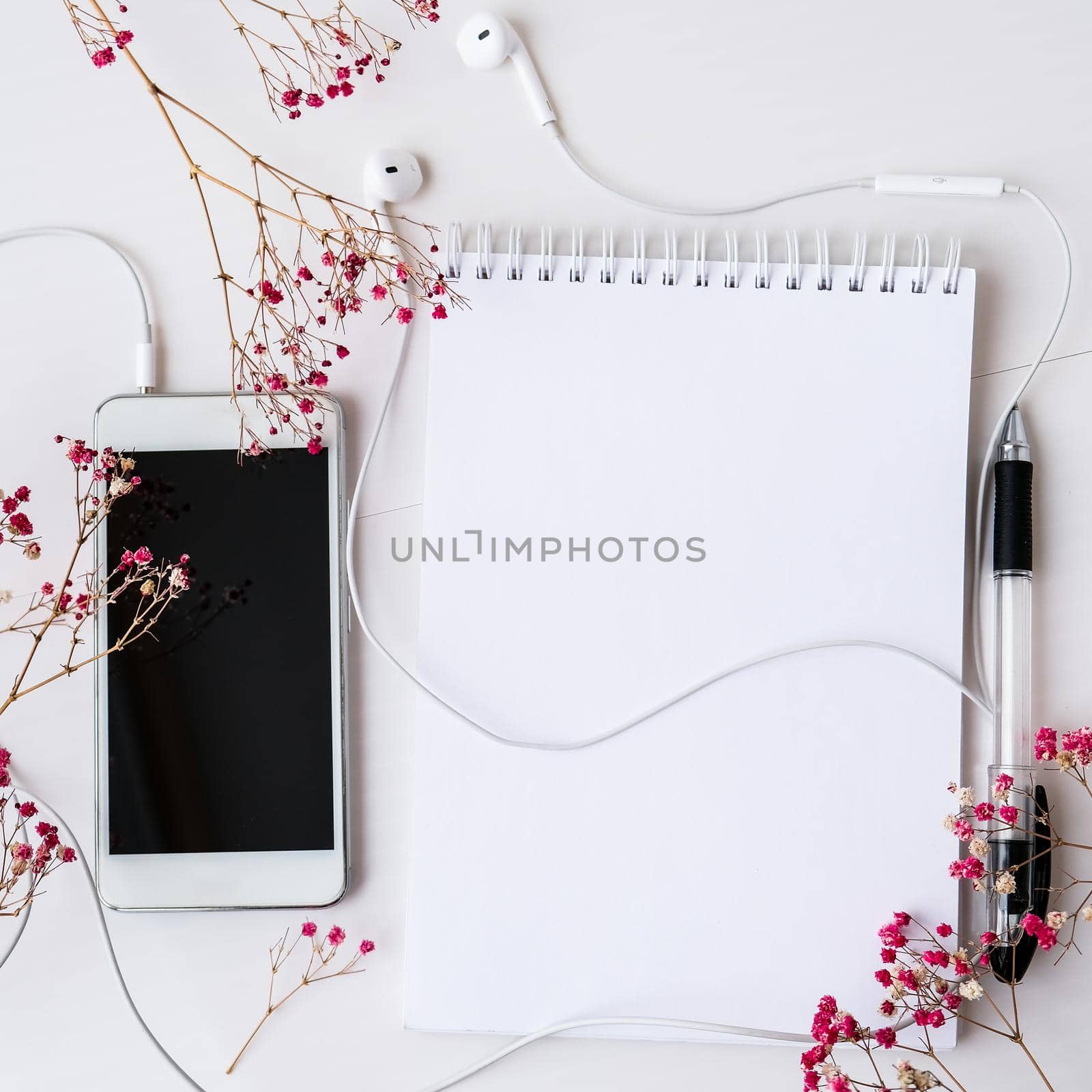 Open blank notebook with headphones mobile phone. Black screen and black pen. Dry pink flowers decoration. Workplace. Copy space foe text. Top view. Pastel colors