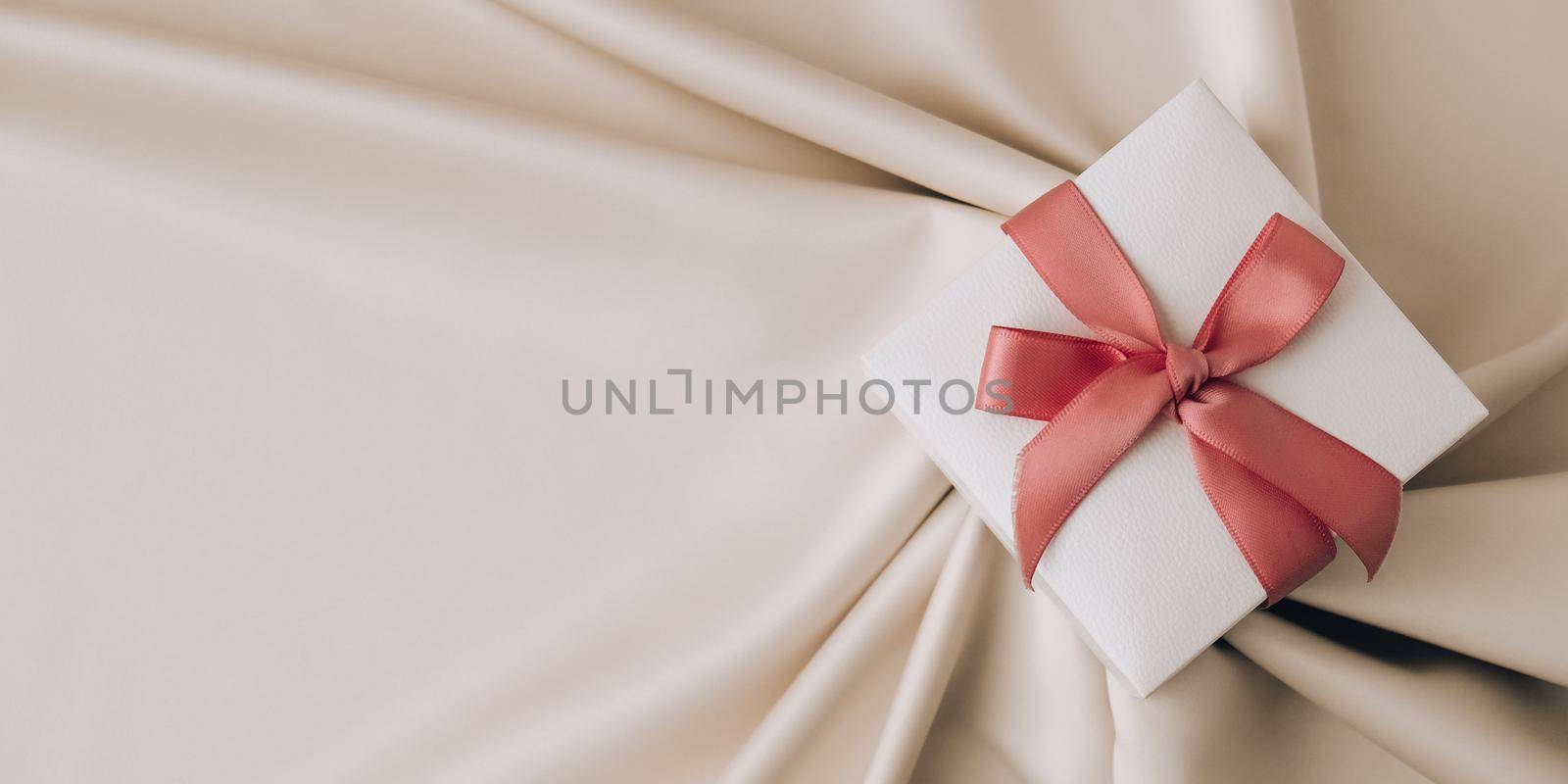 Gift box with pink ribbon on white fabric silk background. Top view, minimal. Present. Copy space. Holiday background. Valentines Birthday Womans Mothers day