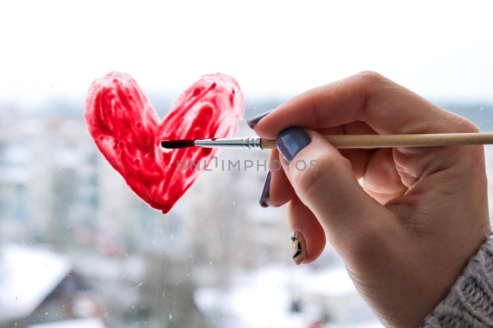 Hand of a girl with a paintbrush painting red heart on a window, stay home, quarantine leisure, let's all be well, Valentines day, Love, Romance