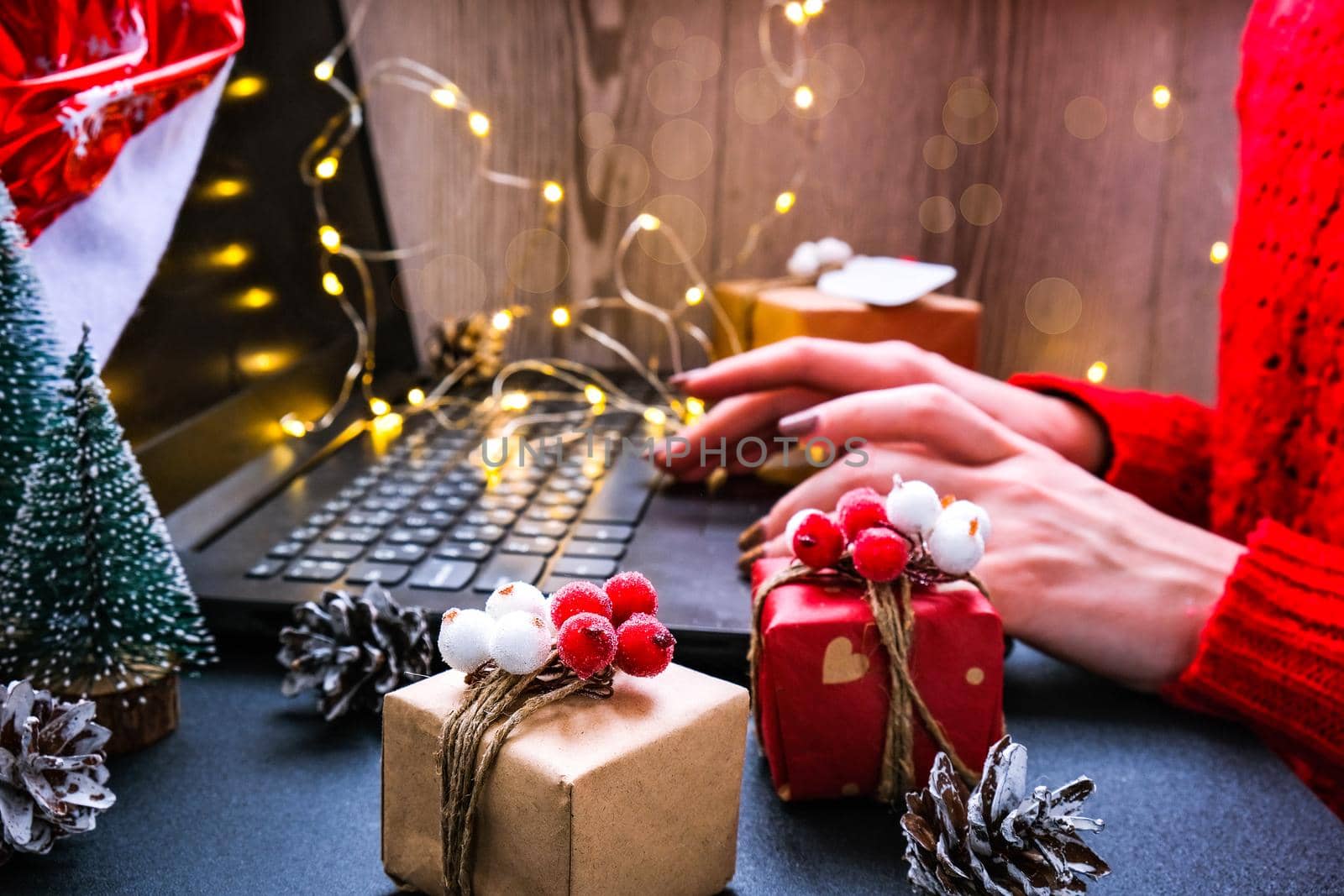 Christmas online shopping, work and education. New Year decorations on table. Woman with notebook computer at home. Winter holidays sales. Gift boxes, christmas trees. Garland light