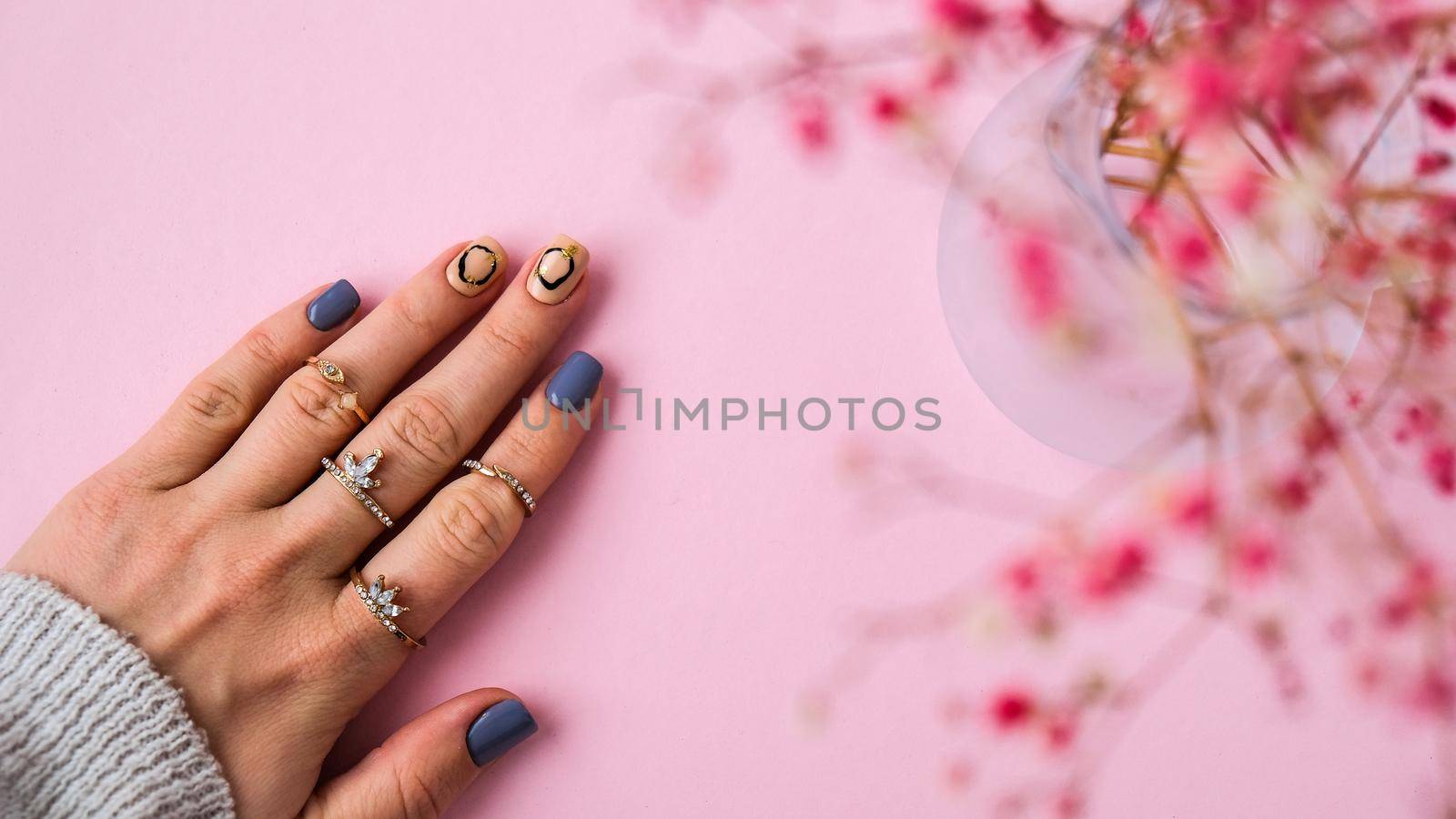 Hand in sweater and pink flowers with modern manicure nails. Female hand. Glamorous beautiful manicure. Manicure salon concept. Nail polish close up.