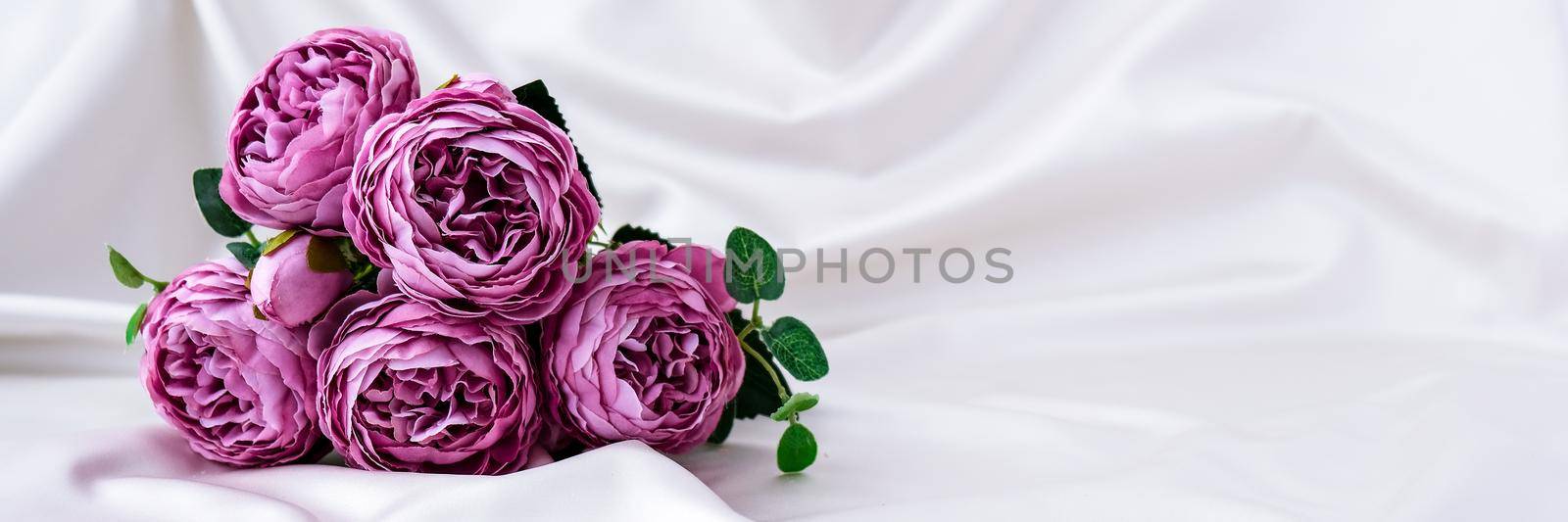 Bouquet of beautiful violet peonies on white silk fabric background. Copy space. Greeting card. Flowers for present