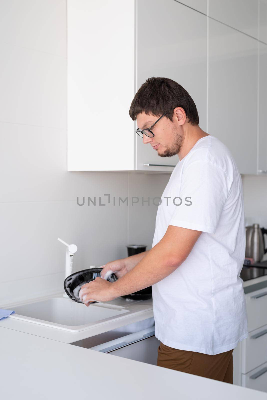 Doing chores. Man in white shirt washing dishes in the modern kitchen. Minimal modern kitchen interior