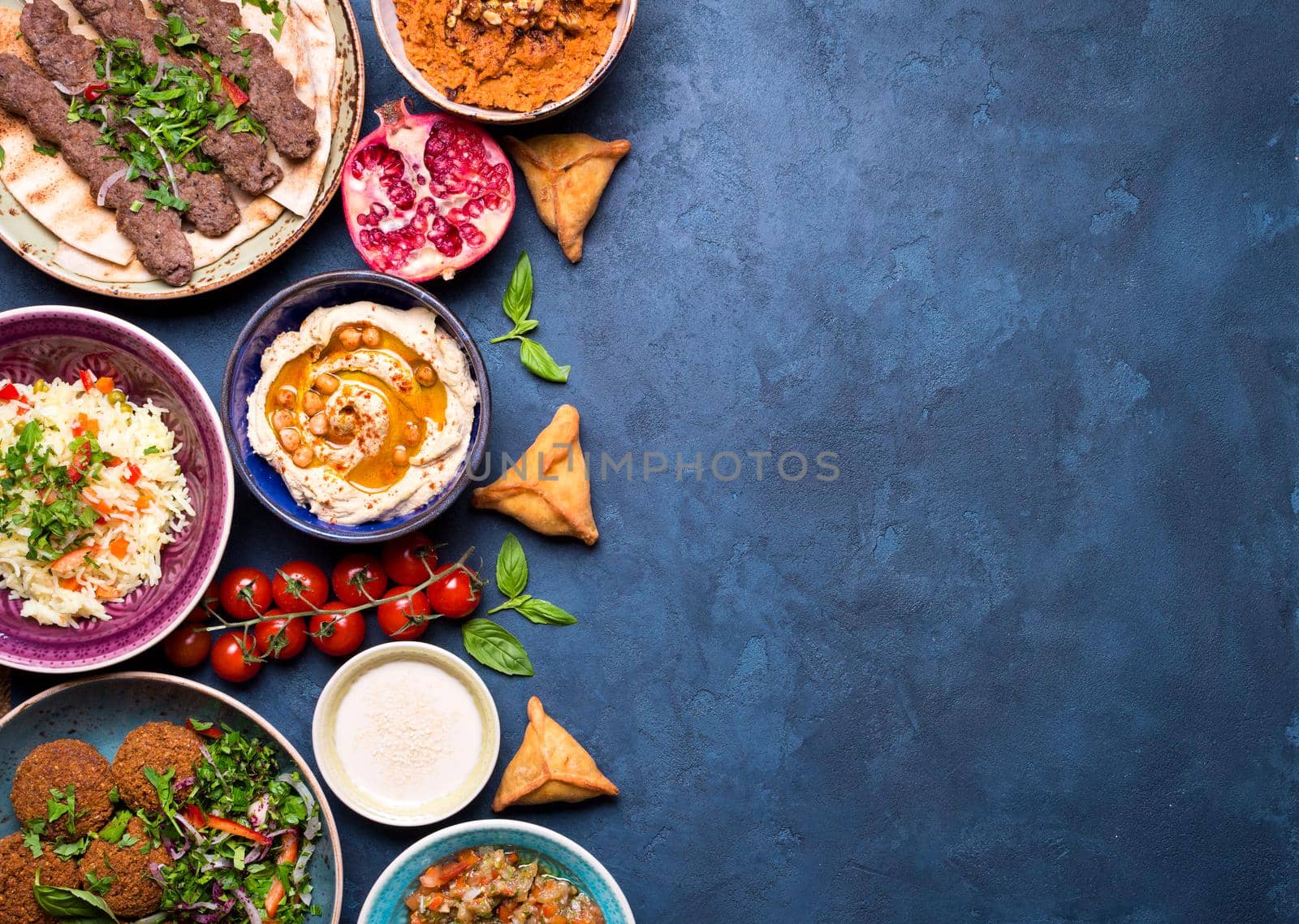 Middle eastern or arabic dishes and assorted meze on concrete rustic background. Meat kebab, falafel, baba ghanoush, hummus, sambusak, rice, tahini, kibbeh, pita. Halal food. Space for text. Top view