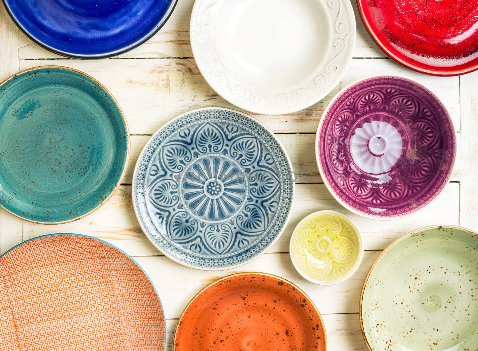 Different antique vintage multicolored empty plates and bowls on a white old wooden table. Table setting. Shabby chic/retro style. Top view. Tableware. Rustic kitchen. Set of plates. Toned image