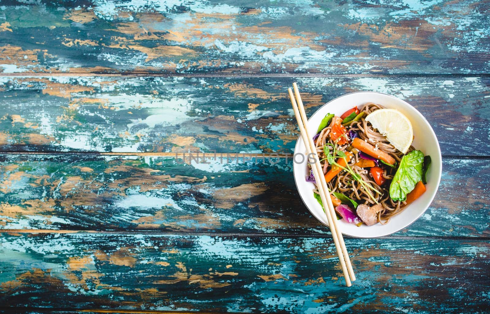 Asian noodles with vegetables, bowl, rustic wooden old background. Space for text. Top view. Soba noodles, vegetables, mushrooms, chopsticks. Vegetarian/Vegan noodles. Asian style dinner with noodles