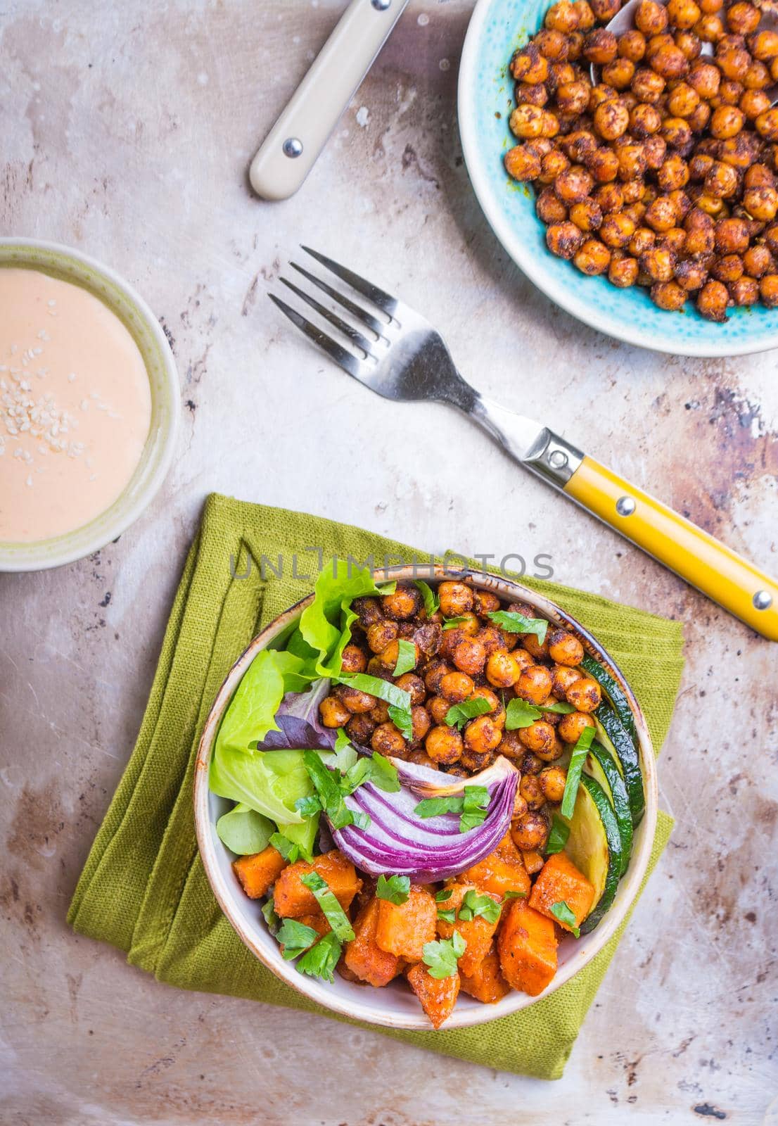 Healthy vegetarian salad with vegetables, sweet potato, chickpea, salad leaves. Healthy buddha bowl salad, sauce, fork. Vegan or vegetarian food. Healthy lunch/dinner. Salad in bowl on table. Top view