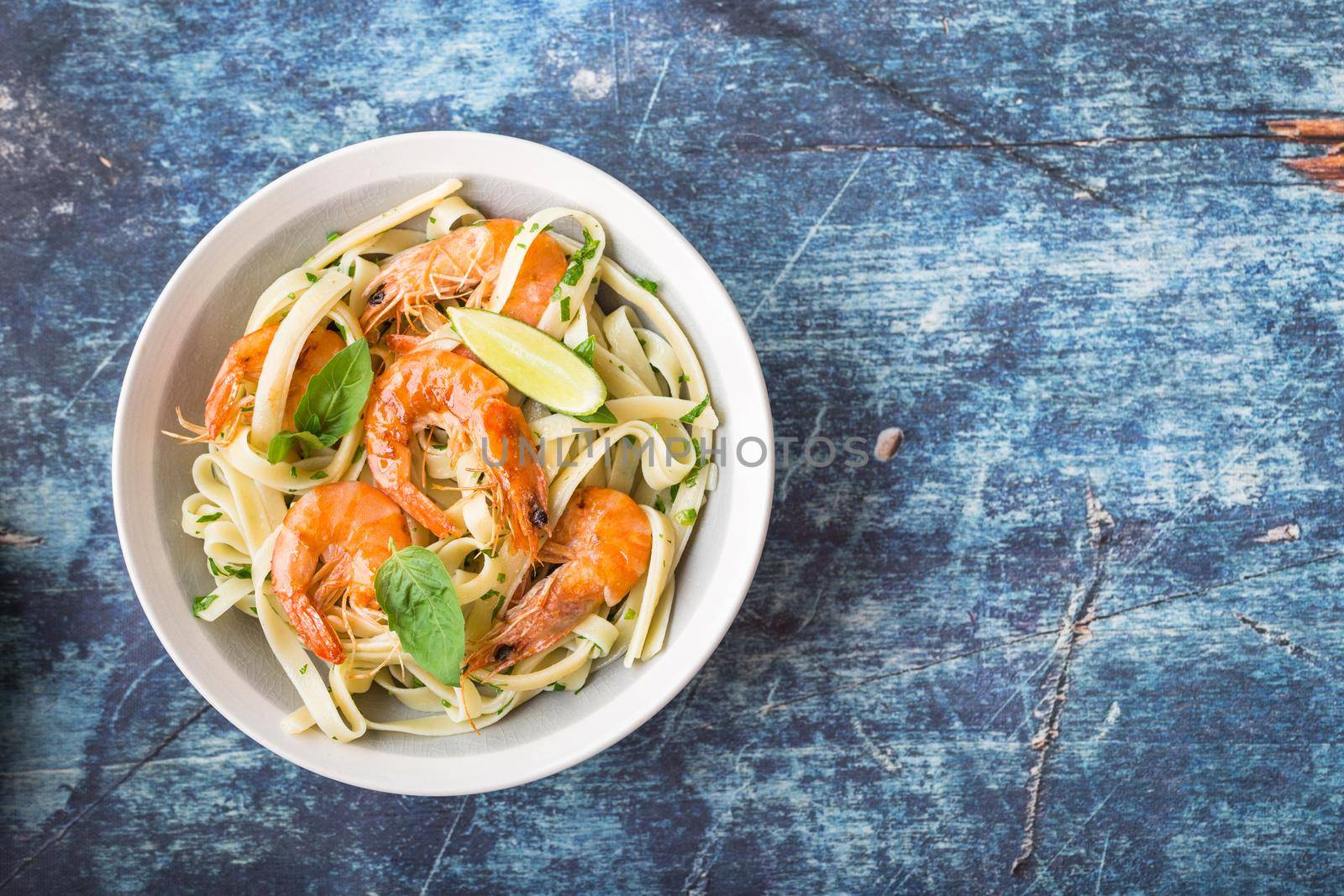 Homemade pasta with fried shrimps and basil on rustic wooden blue background. Space for text. Pasta with seafood in plate. Top view. Closeup. Mediterranean cuisine. Pasta for dinner or lunch. Overhead